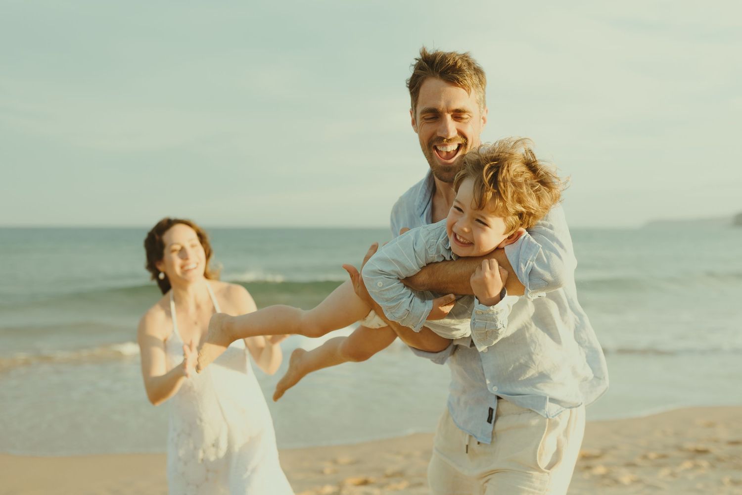 A family shares playful moments running and laughing on the beach at sunset.