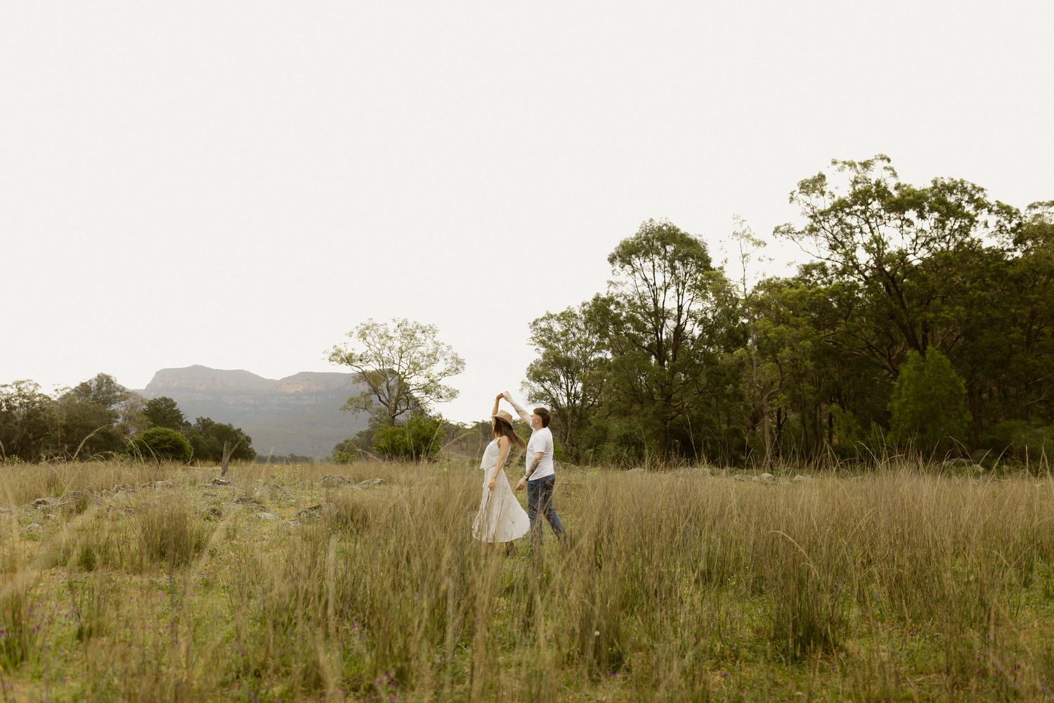 Distant figures in white stand together in a vast grassy field with mountains in the background.