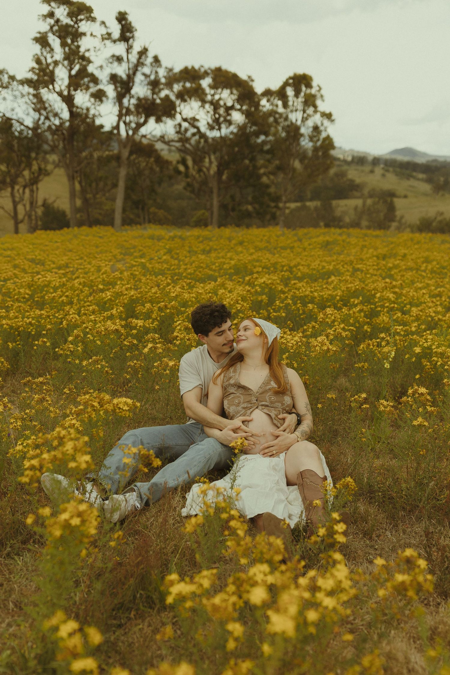 A romantic moment captured in a field of golden wildflowers with rolling hills in the background.