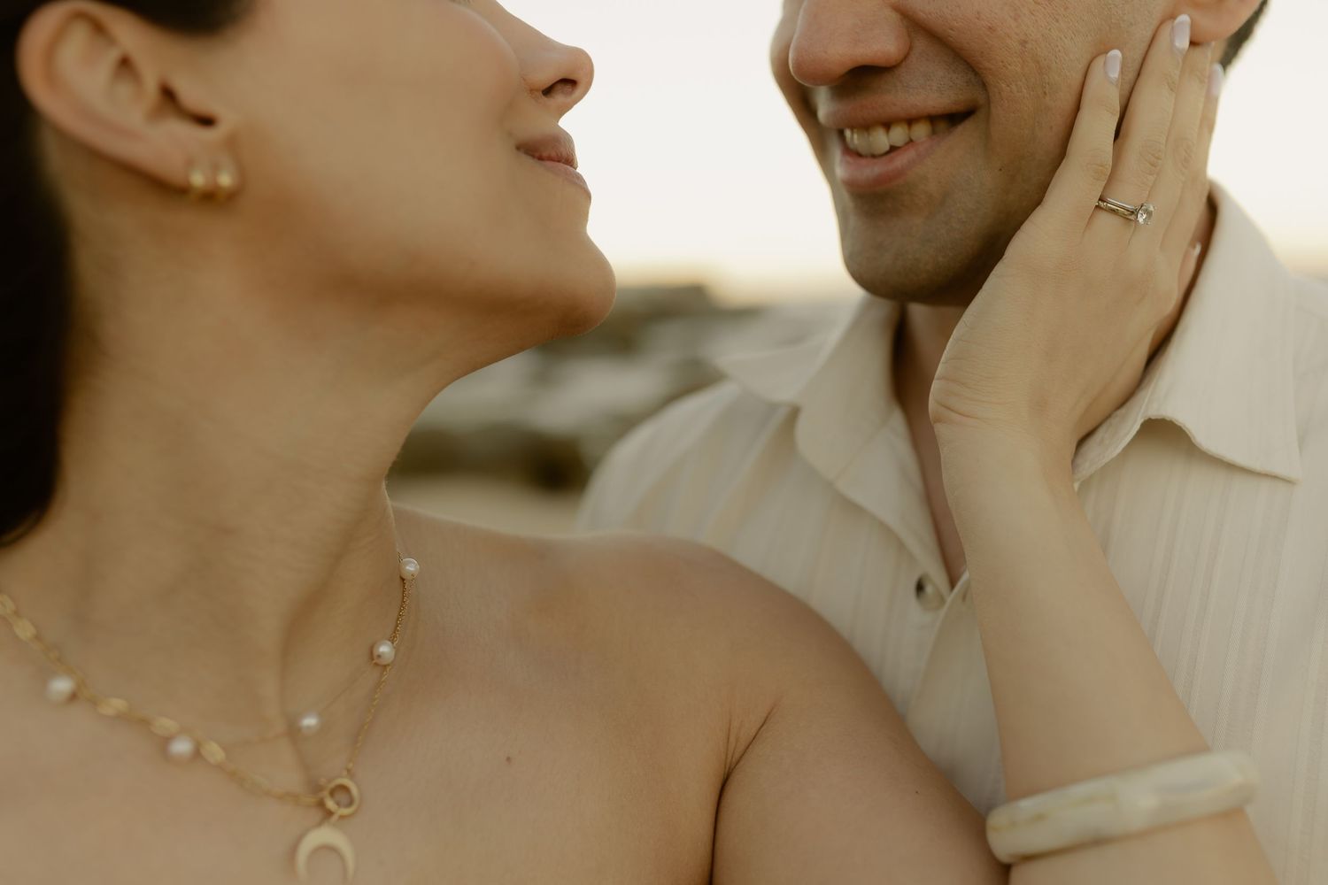 Close-up of smiling couple, woman wearing gold necklace and bracelet, man with engagement ring.