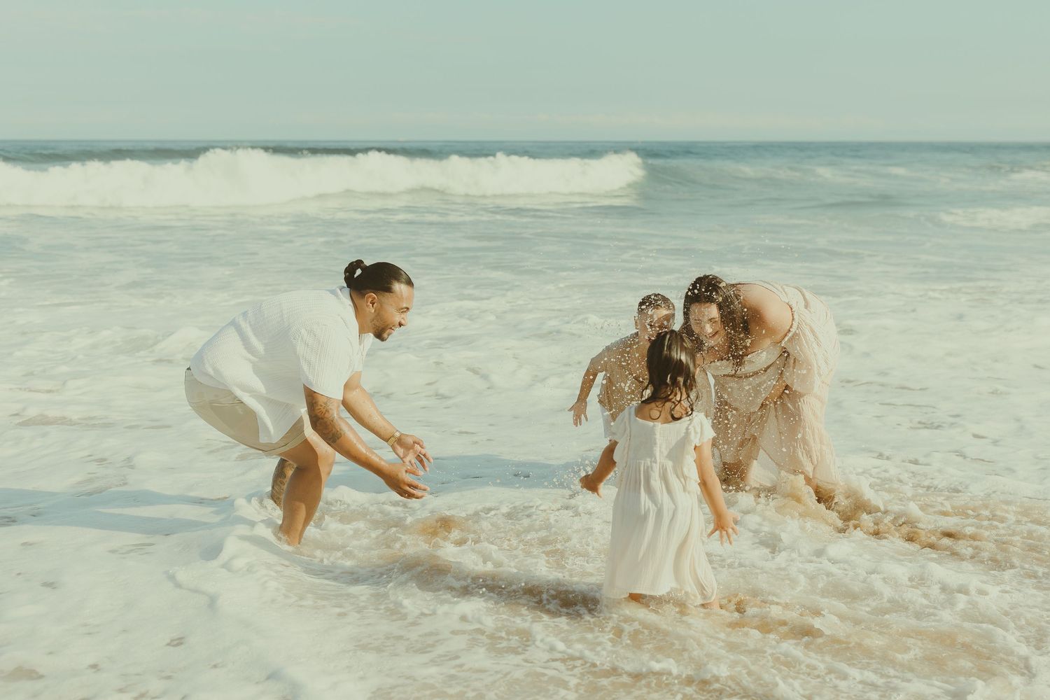 A group plays in the ocean waves at sunset, splashing and running along the sandy beach.