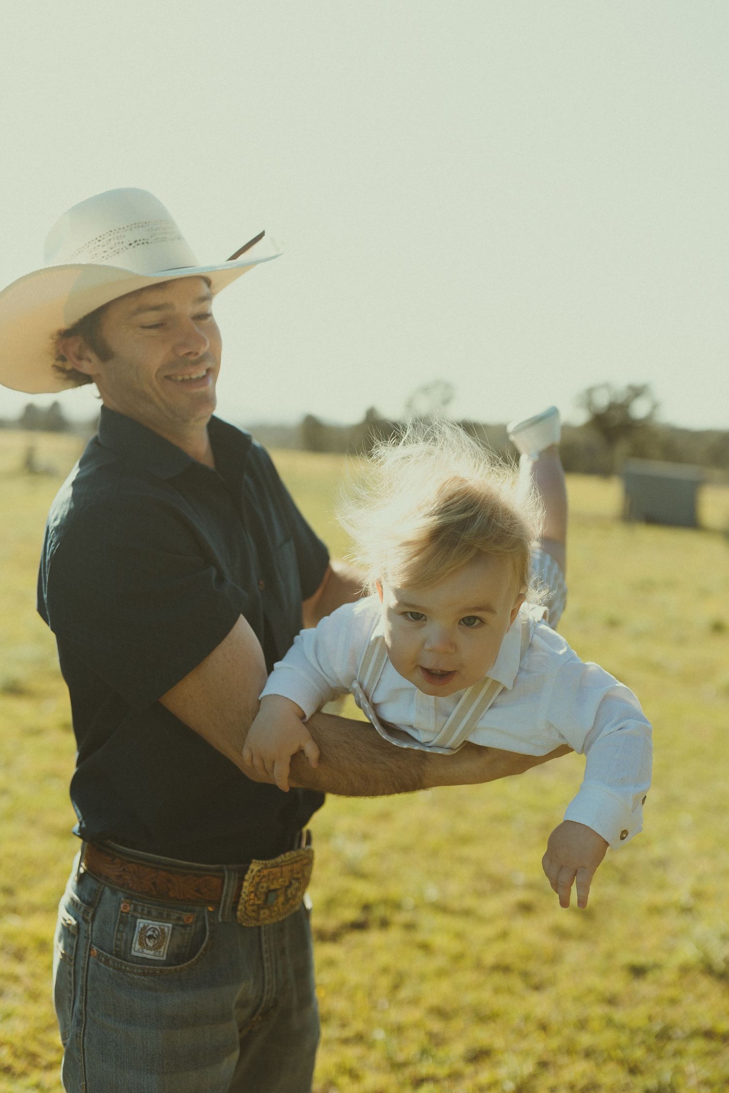 Playful sequence of a parent swinging and playing with a small child in a grassy field at sunset.