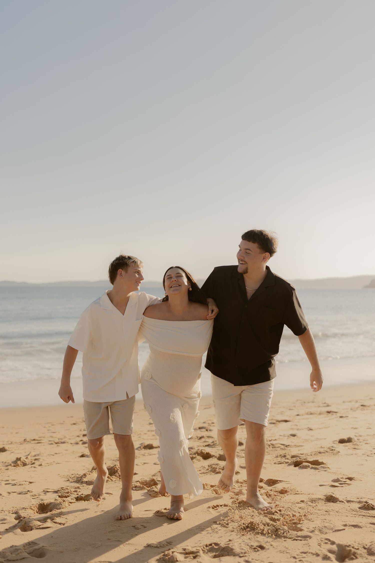 Three people walking together on a sunny beach while holding hands and smiling.