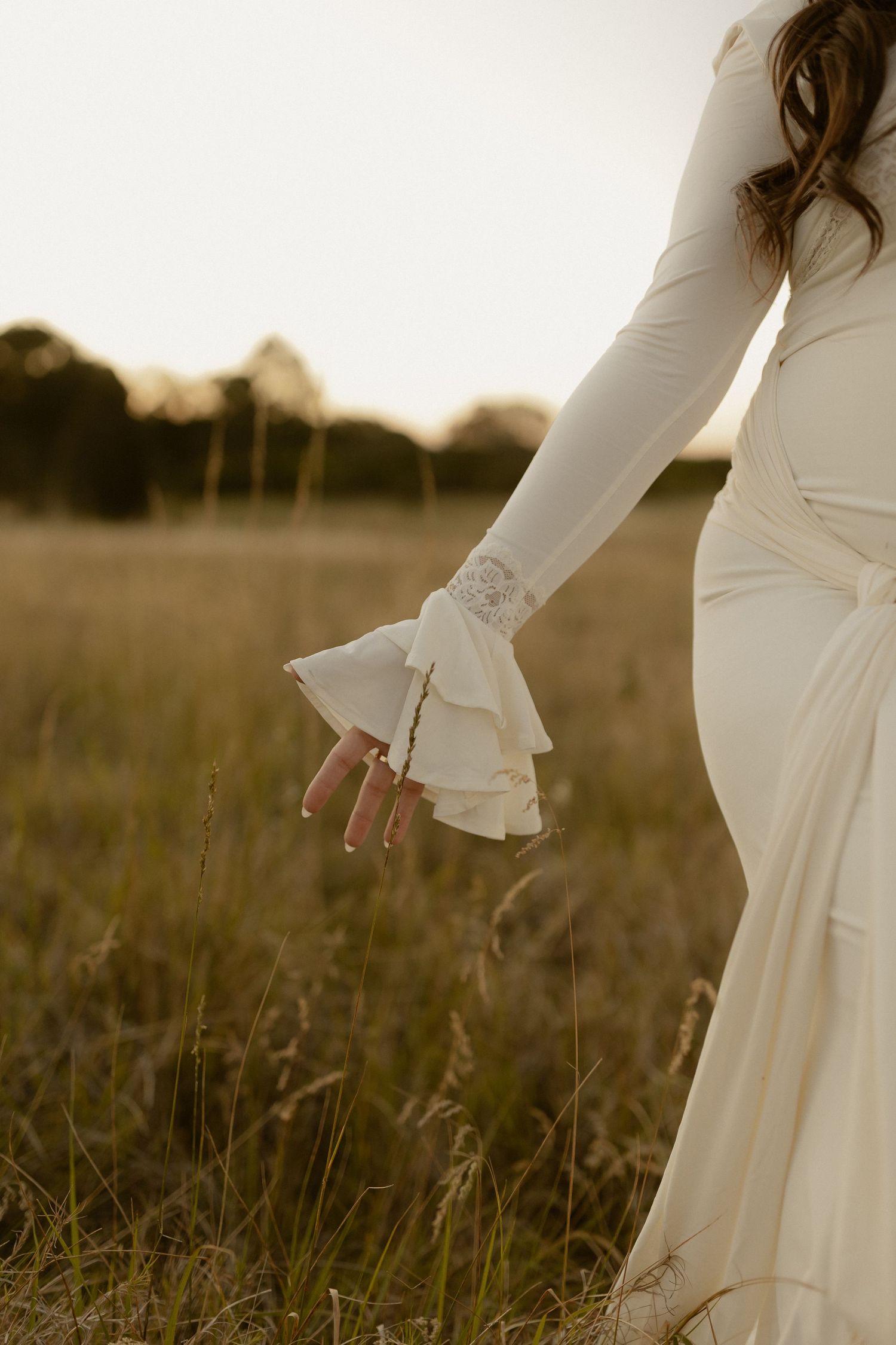 Close-up detail of flowing white maternity dress with bell sleeves against golden grass.