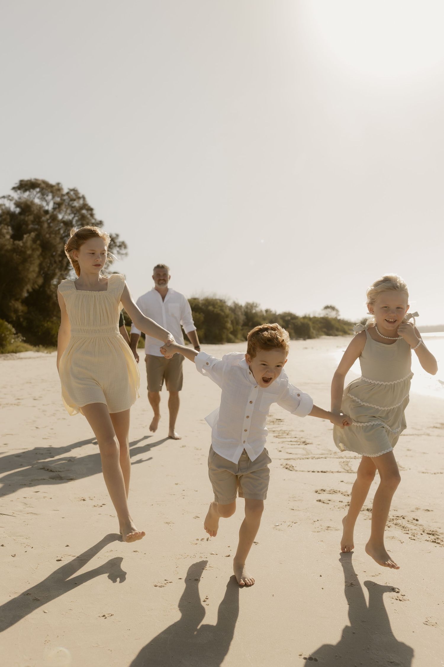 A family runs and jumps together along the shoreline during a beach photoshoot.