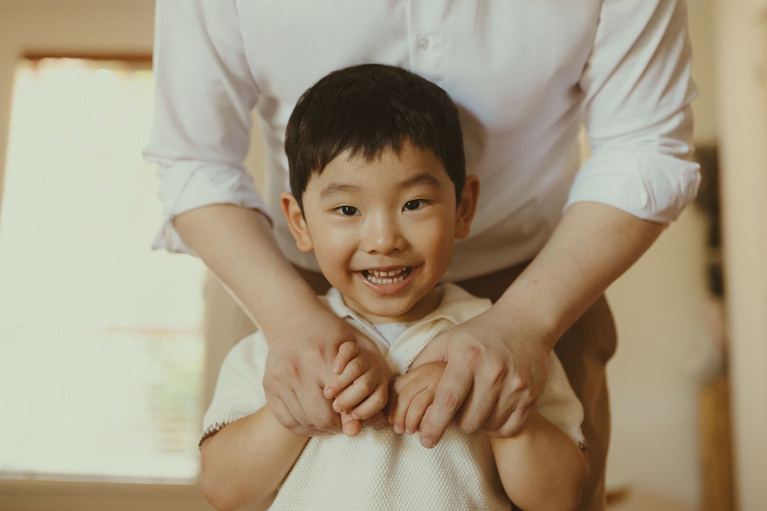 A child and parent practice yoga together on a white mat in a bright room.