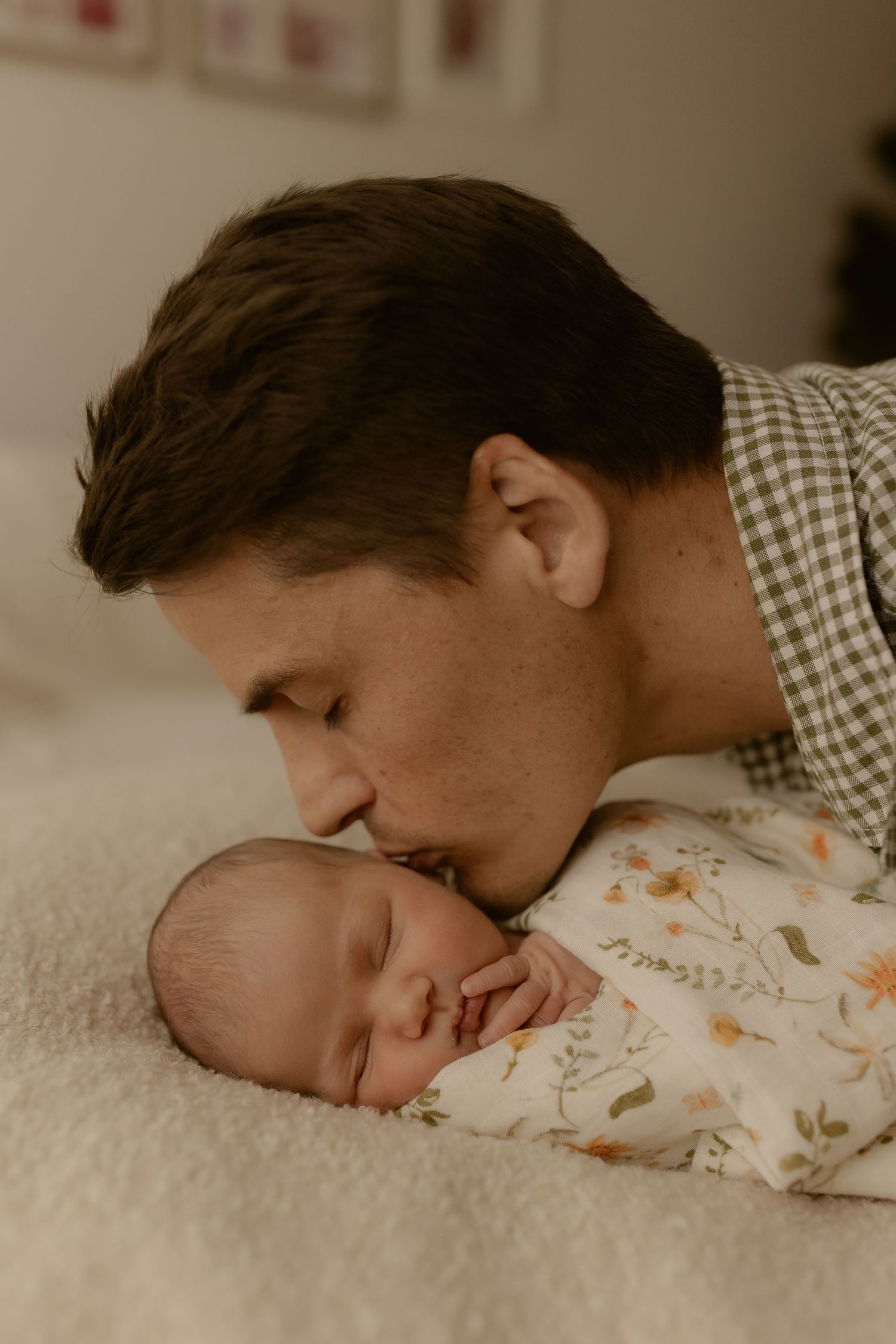 Tender moment between parent and sleeping baby on white blanket in muted tones.