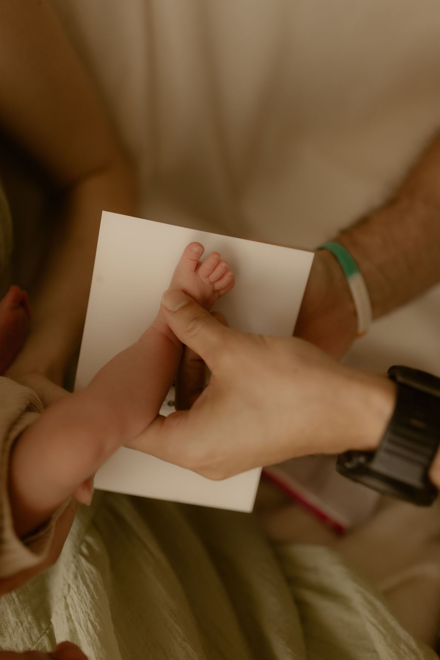 Tiny baby hand being pressed onto white paper for keepsake print in soft lighting.