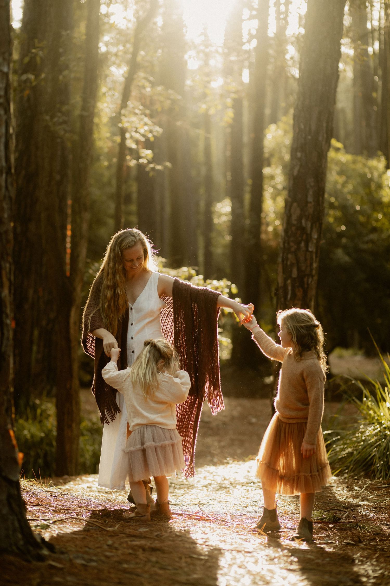 A sun-drenched forest scene shows three figures dancing together among tall trees in golden afternoon light.
