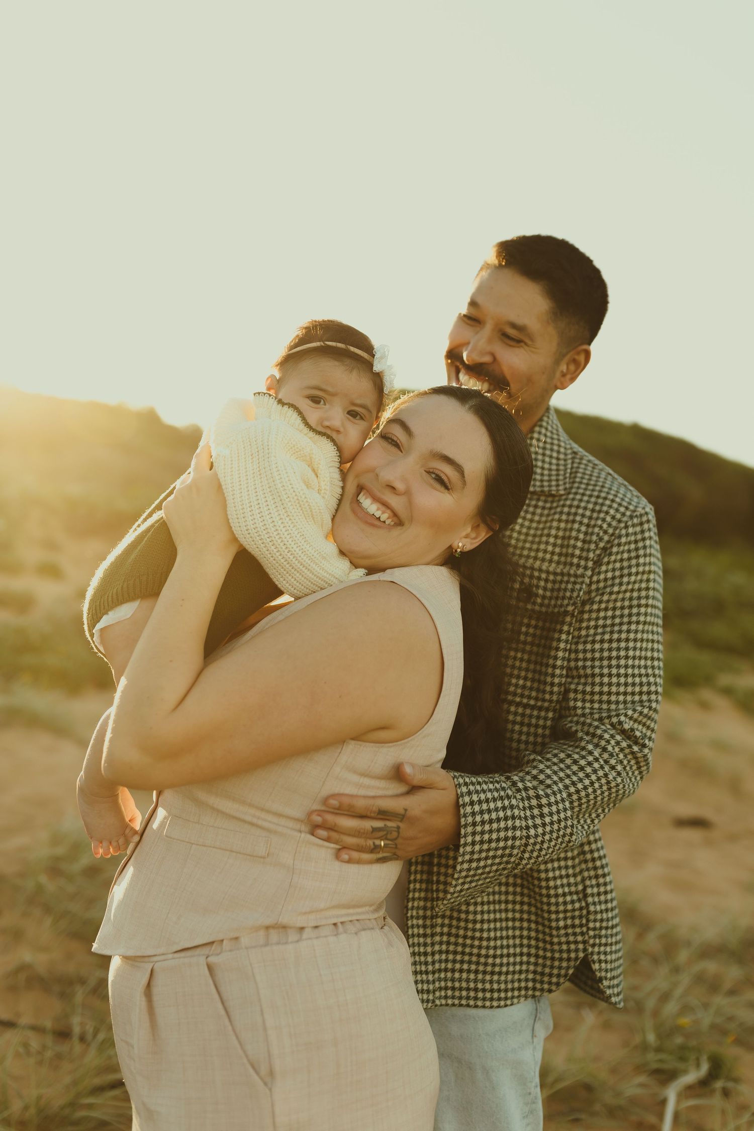 Family embracing outdoors during golden hour sunset in warm tones.