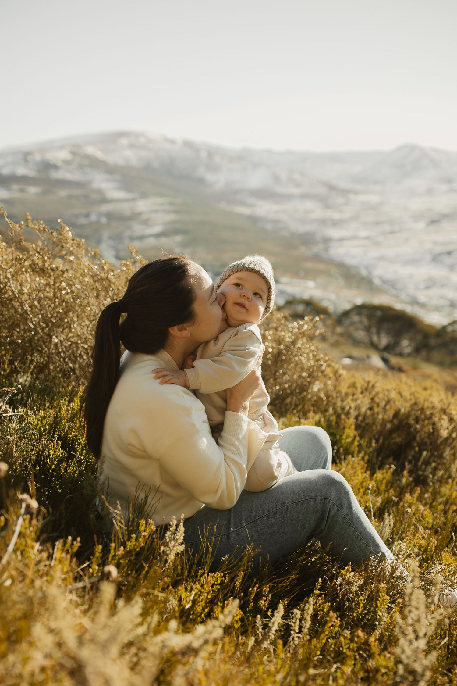 Golden sunset illuminates peaceful mother and child moment in mountain meadow during outdoor portrait session.