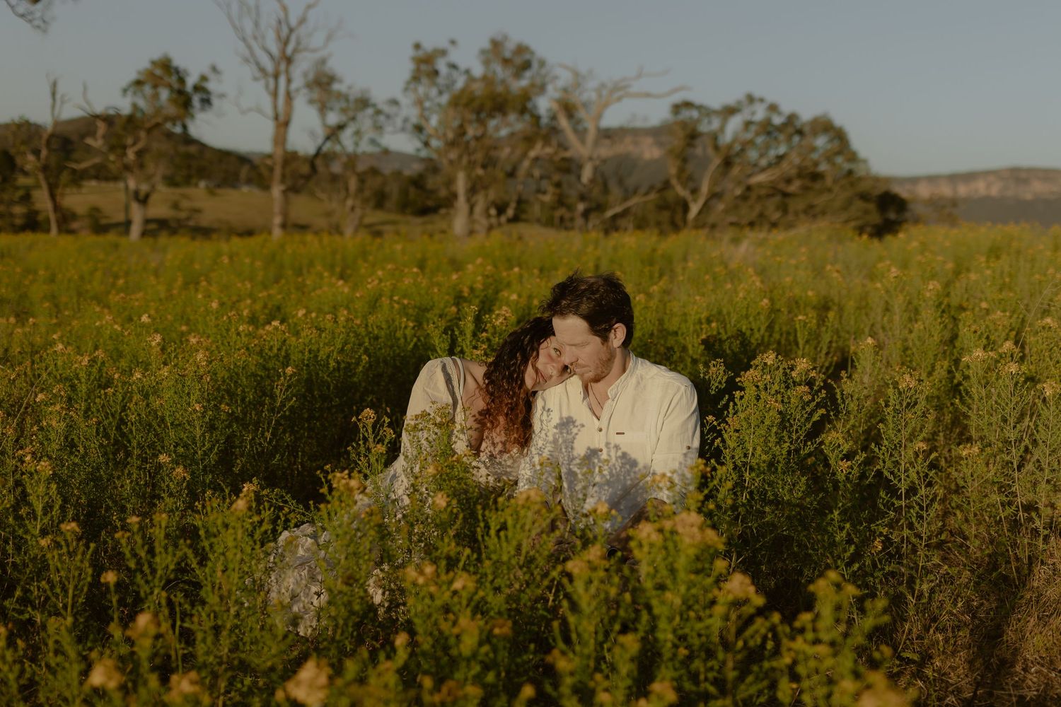 Romantic scene of couple embracing in wild yellow flowers with mountains in distance.