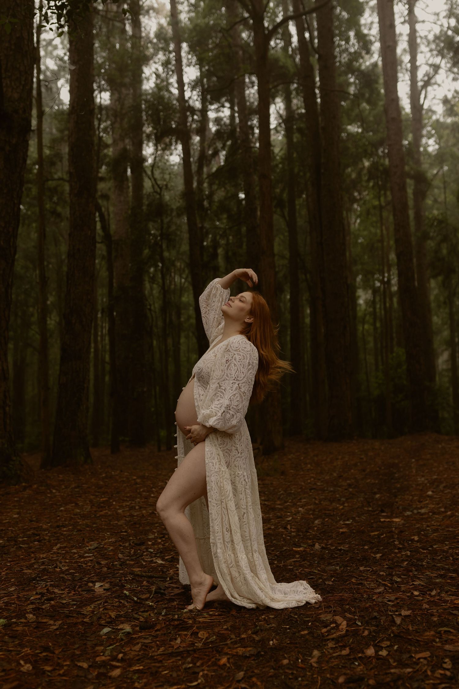 Dreamy forest photoshoot featuring person in vintage lace dress among tall trees.