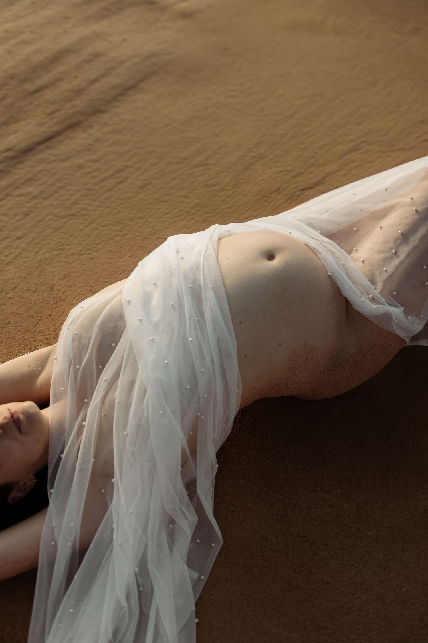 A person lying down wearing a delicate sheer white tulle fabric draped across their torso in an artistic pose.
