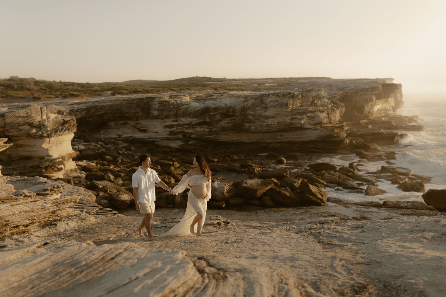Wide panoramic view of rocky coastal cliffs with two figures walking along the rugged landscape.