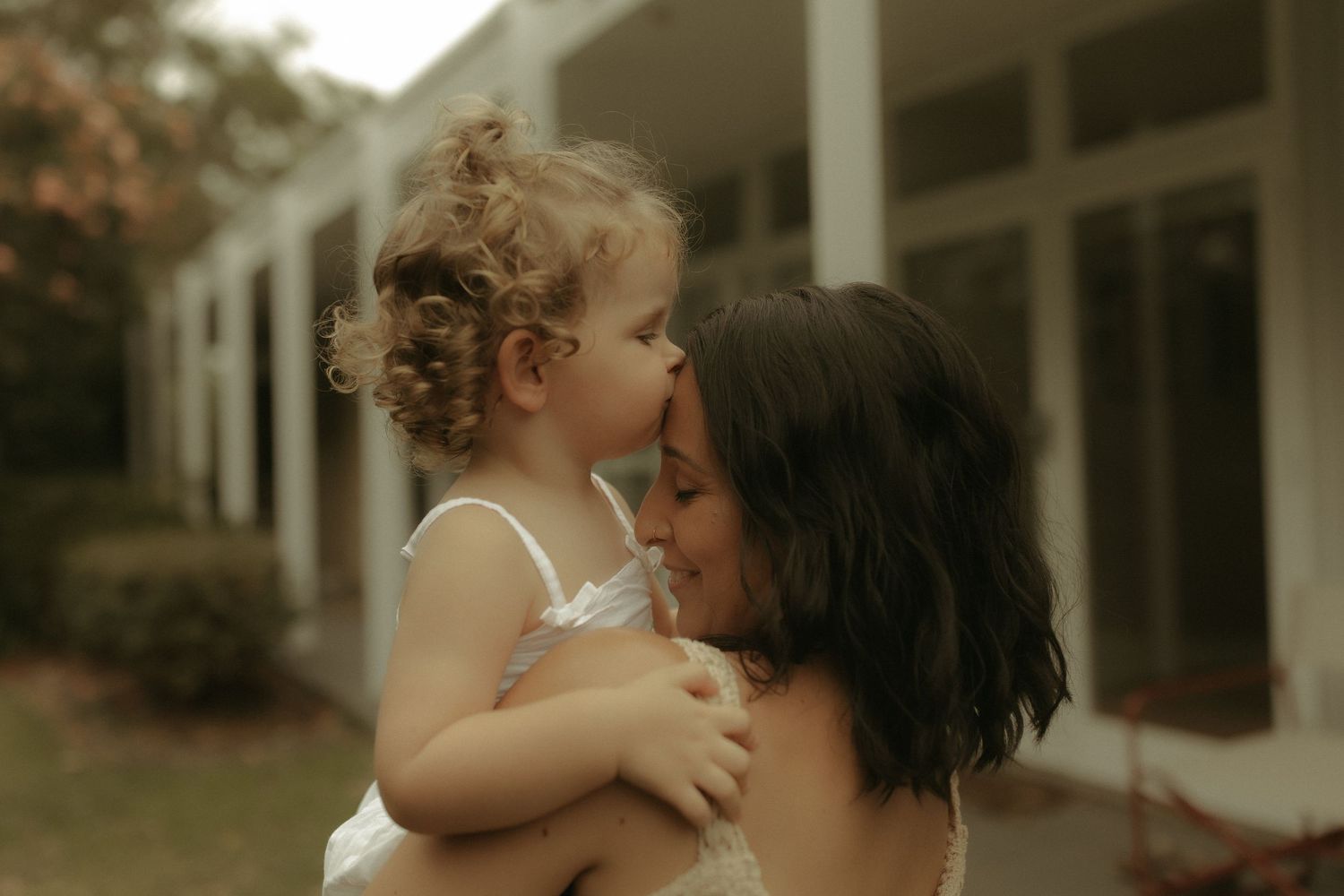 An intimate moment of affection shared outdoors with a modern house in the background.