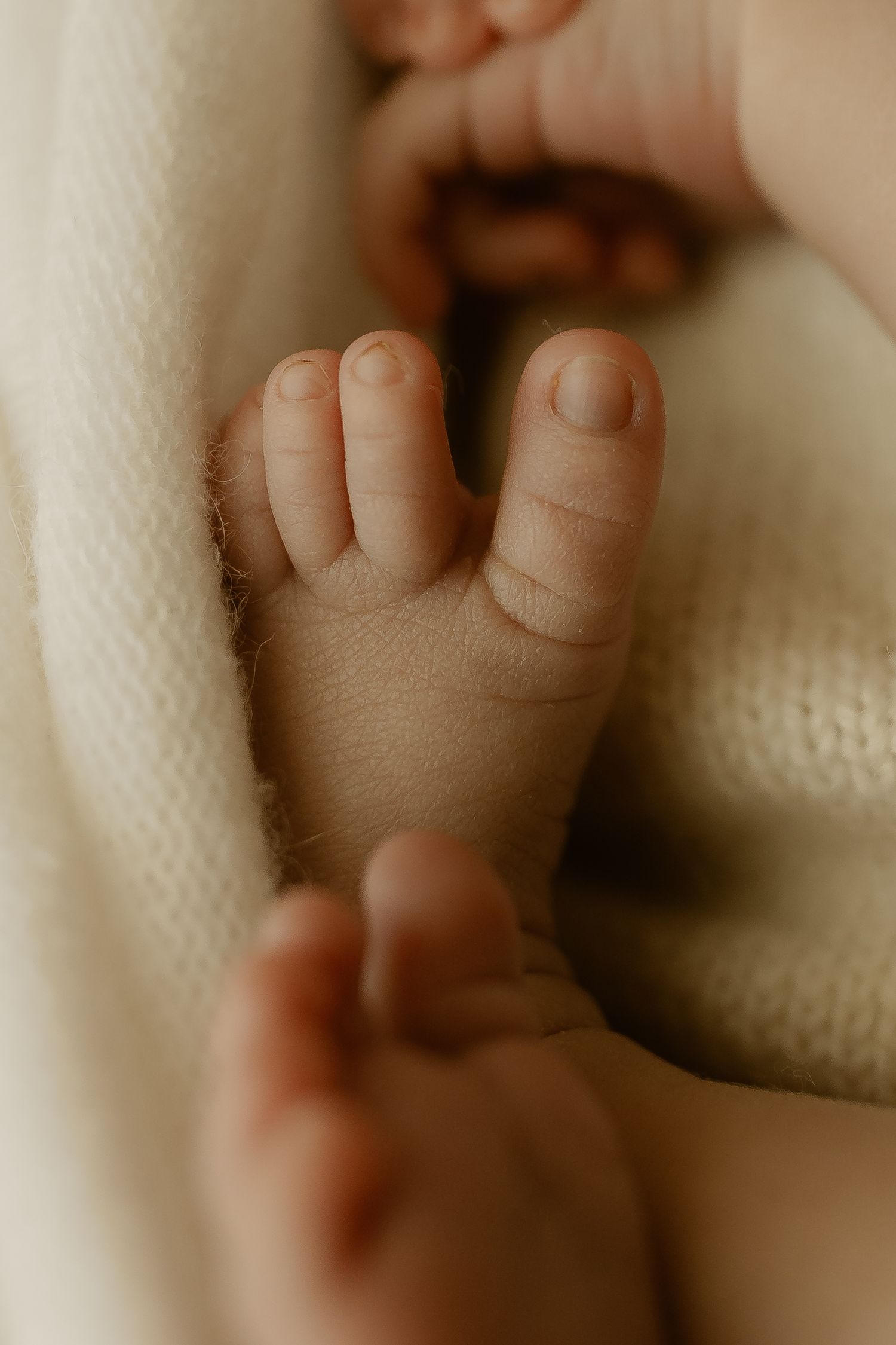 Close-up photo of a tiny baby's fingers grasping a soft white blanket in warm lighting.