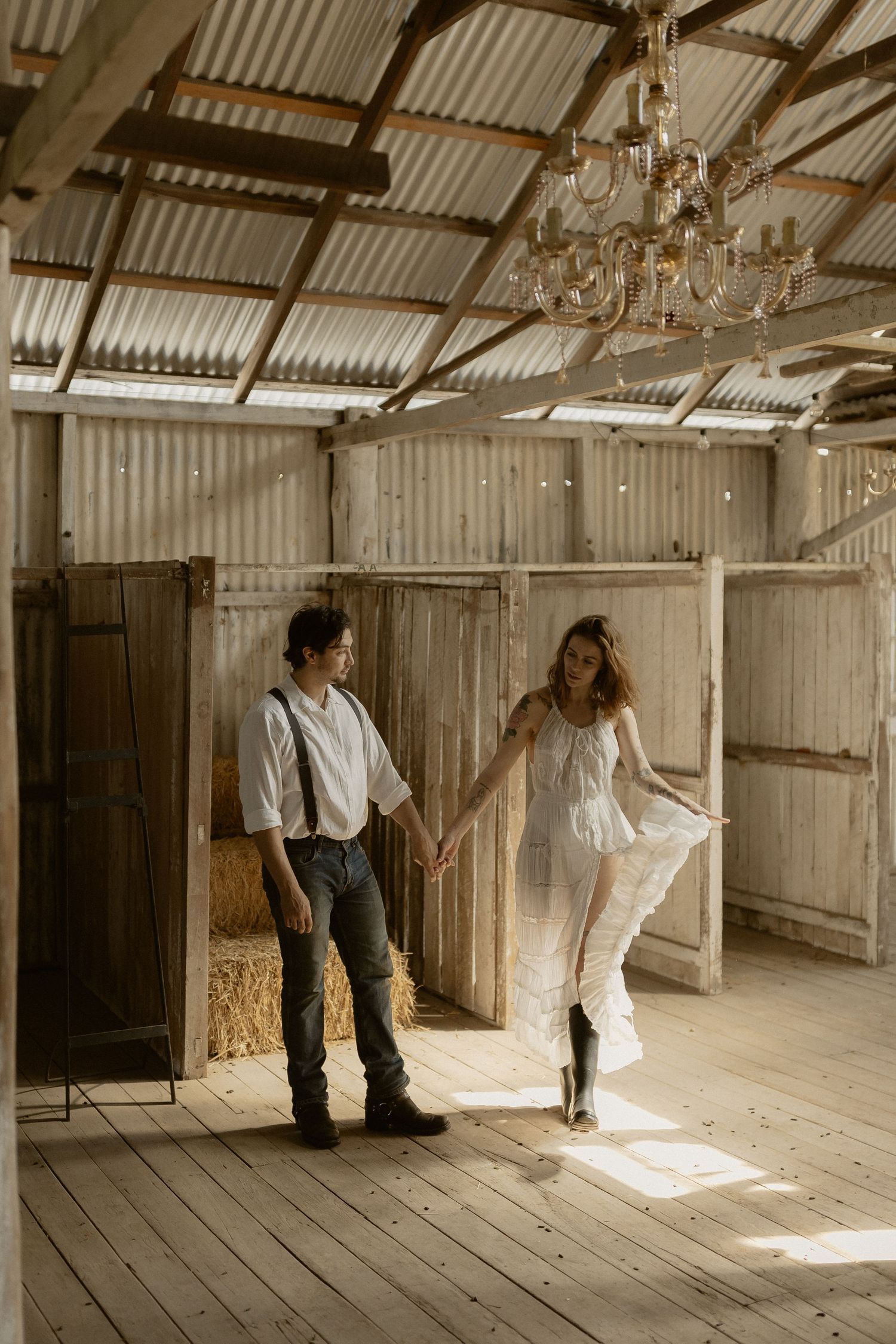A rustic barn interior with wooden floors and corrugated walls features soft natural light streaming through an opening.