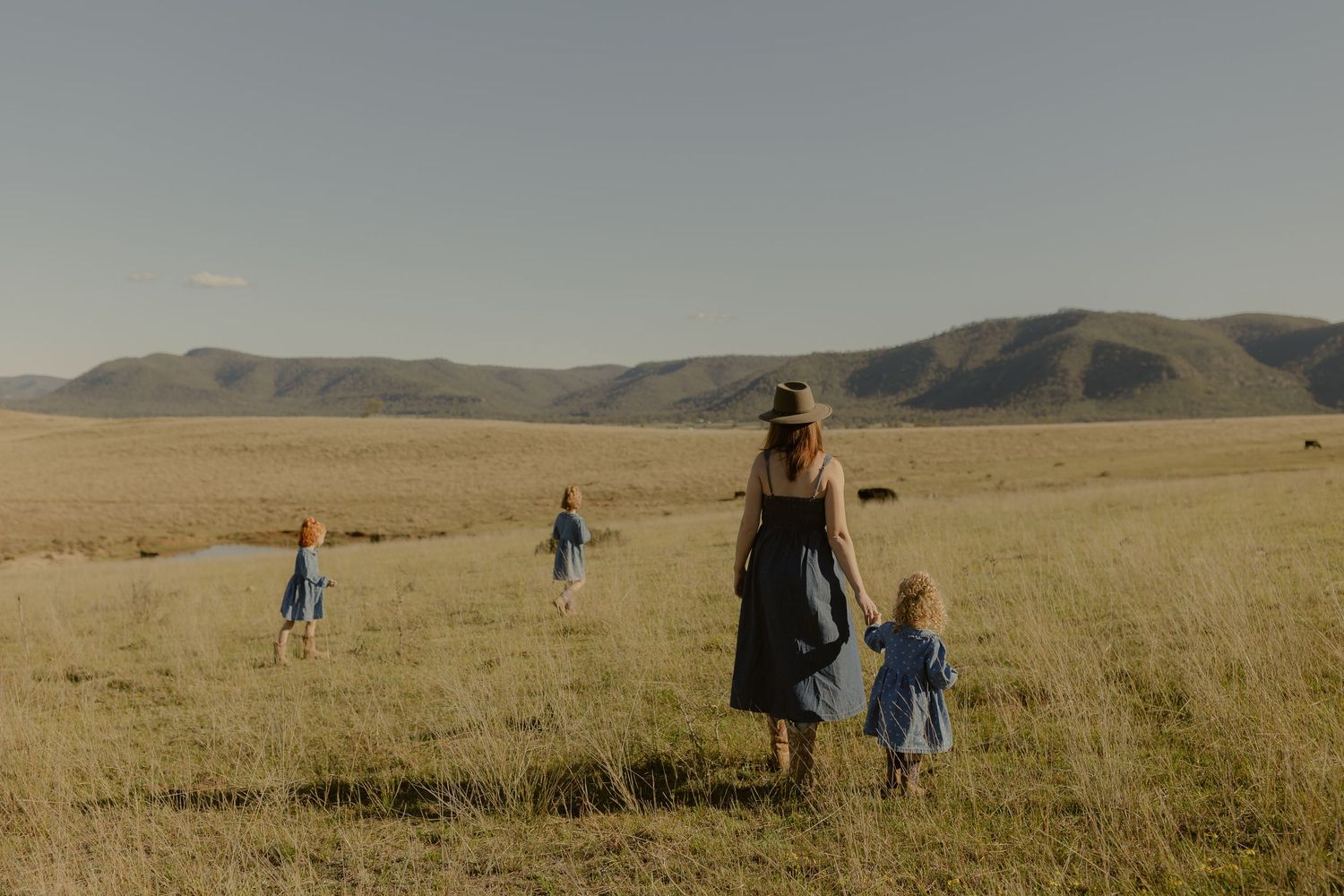 A mother and children walking through a vast golden meadow with rolling mountains in the background.