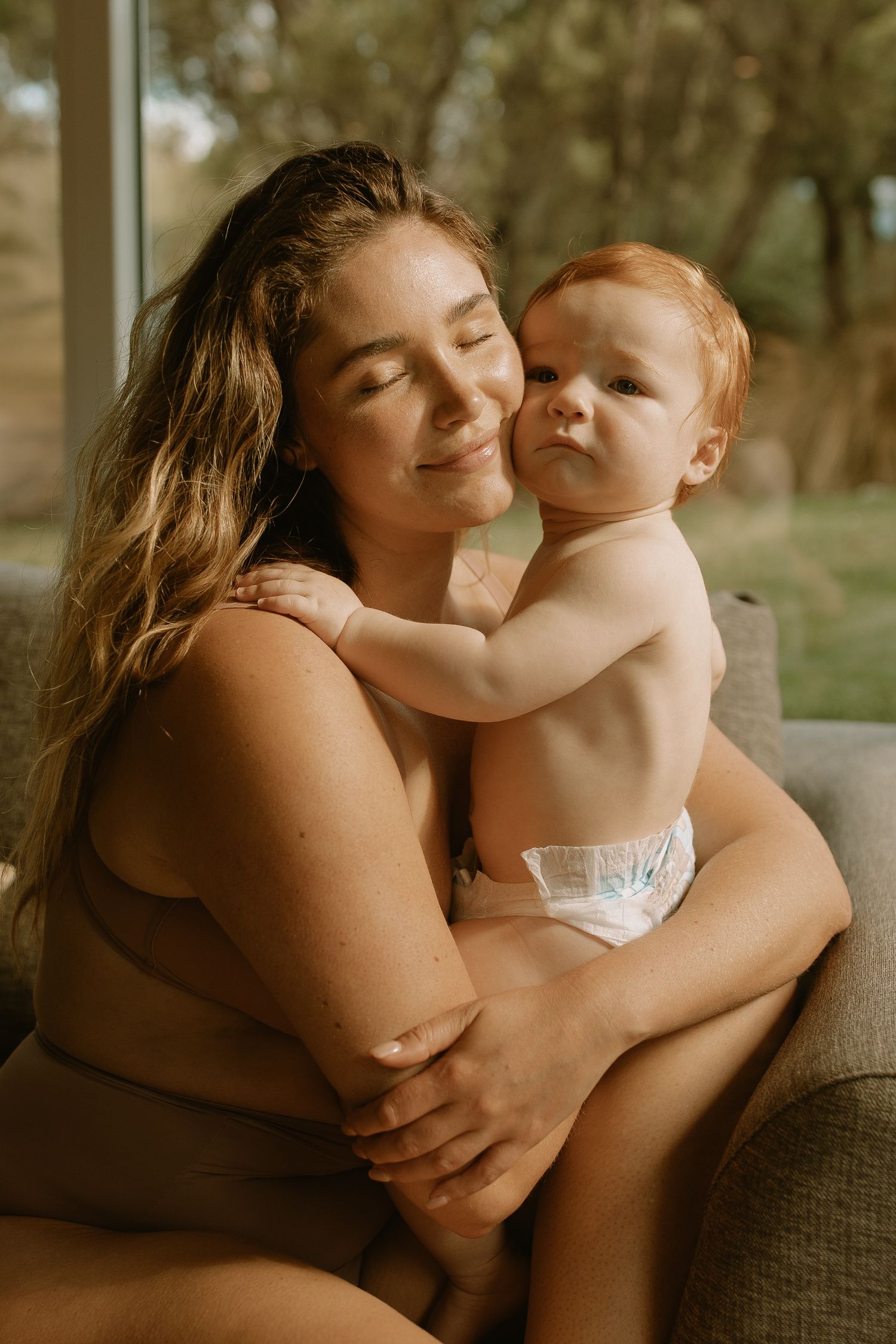 A tender moment between parent and baby in golden sunlight while sitting on a couch at home.