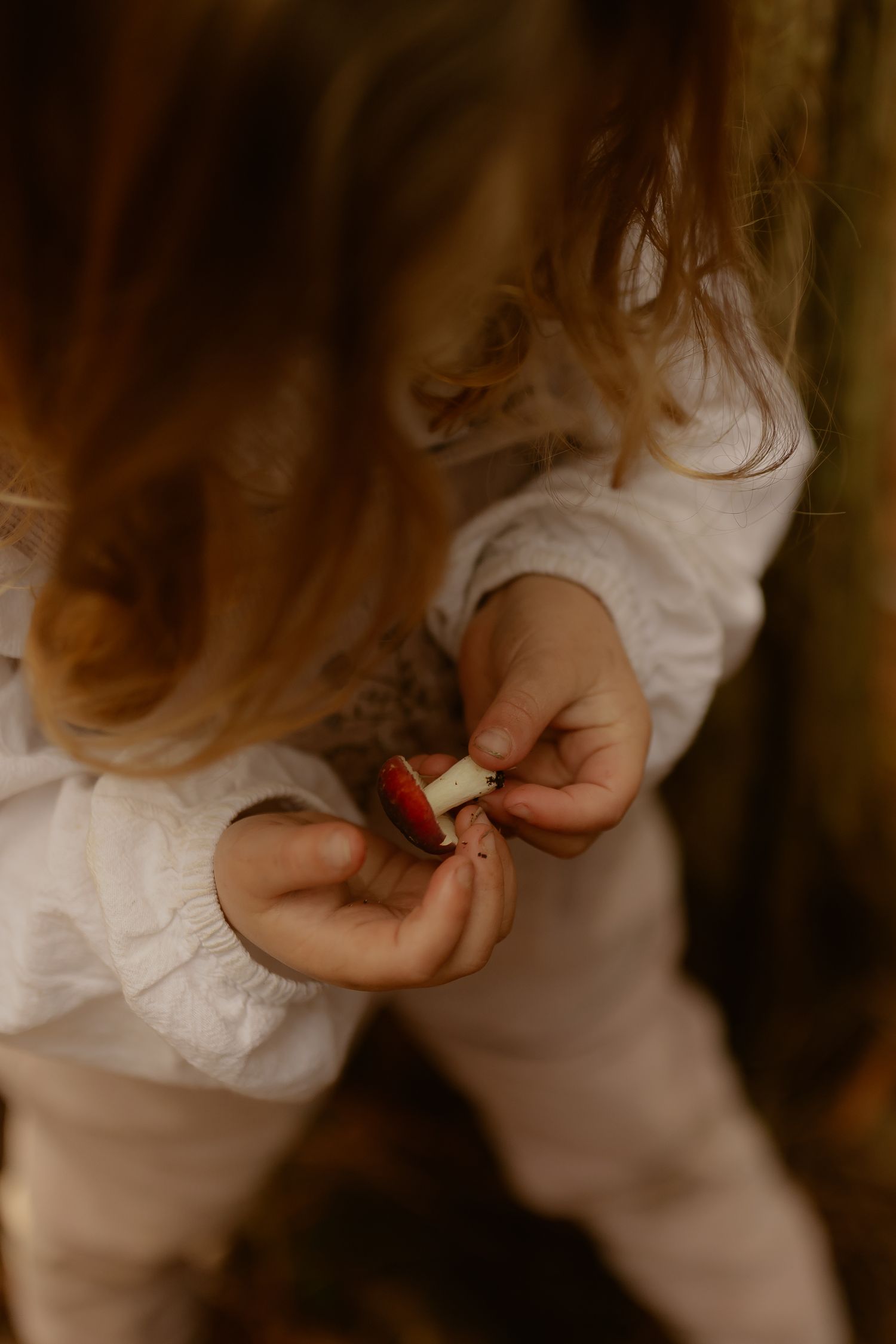 Young child with curly hair holds a small red berry in tiny hands outdoors.
