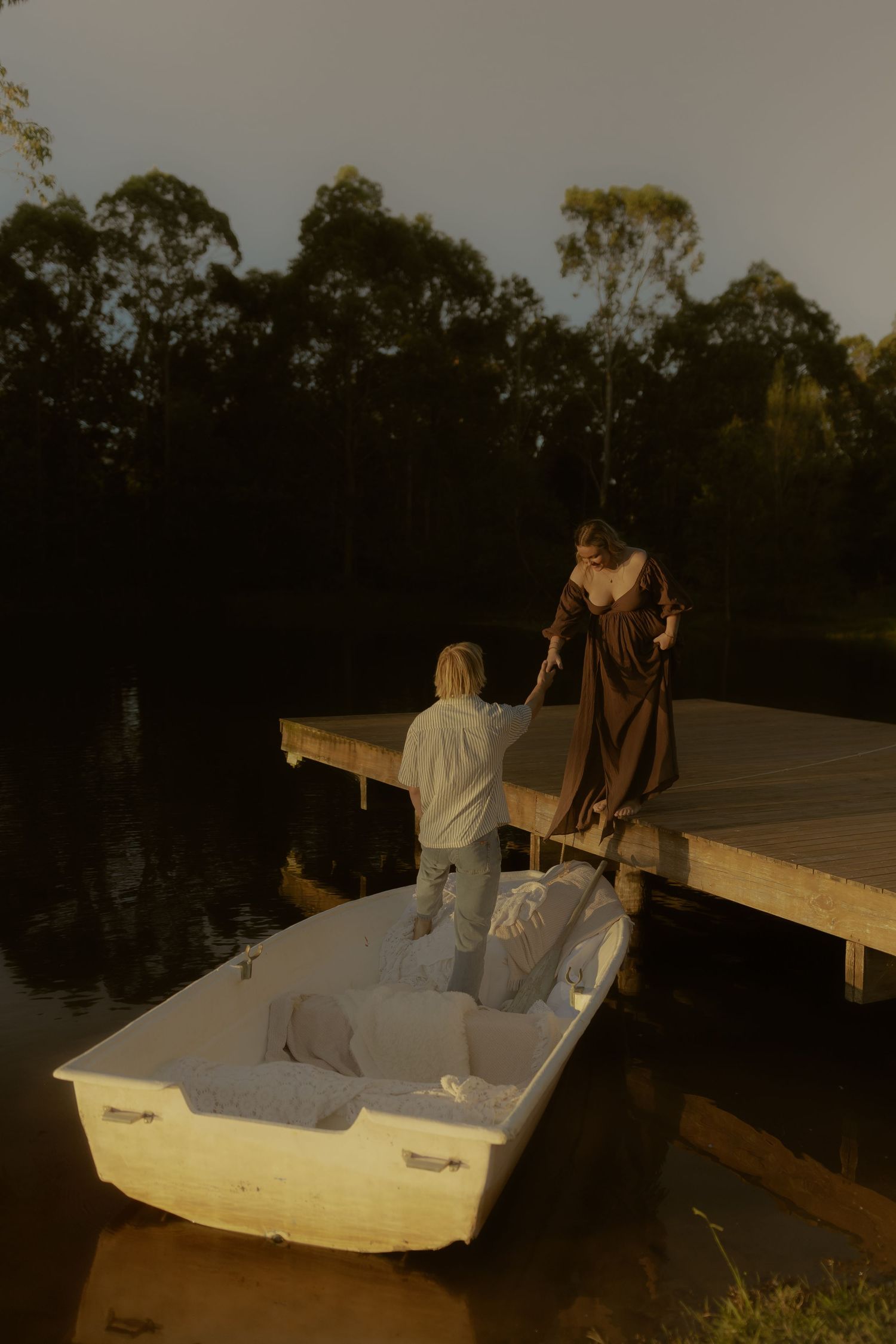 People sitting in a white boat on a lake during sunset with raised arms in celebration.