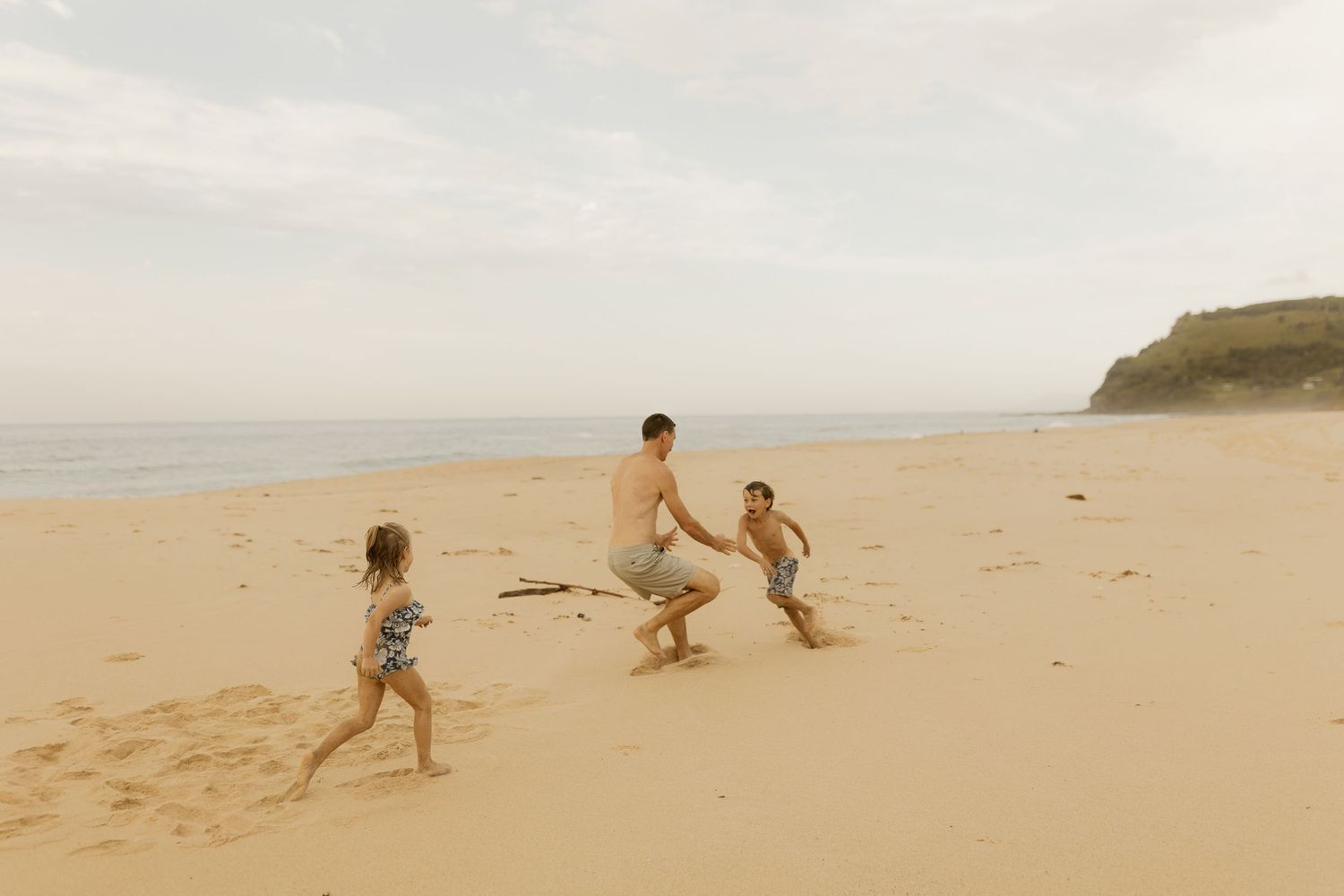 Family playing together on a vast empty beach with coastal cliffs in the background.