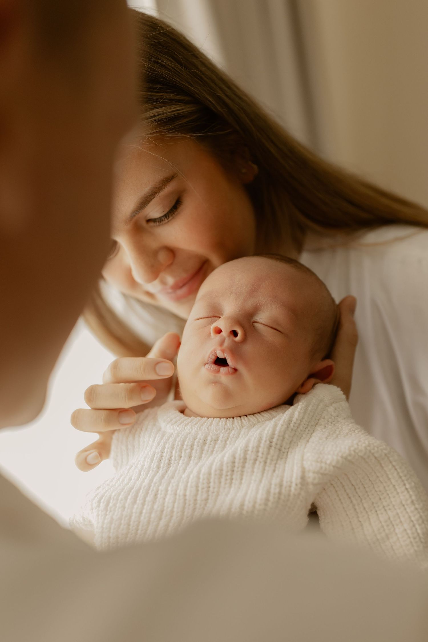 Peaceful newborn in white knit sweater being tenderly held during portrait session.