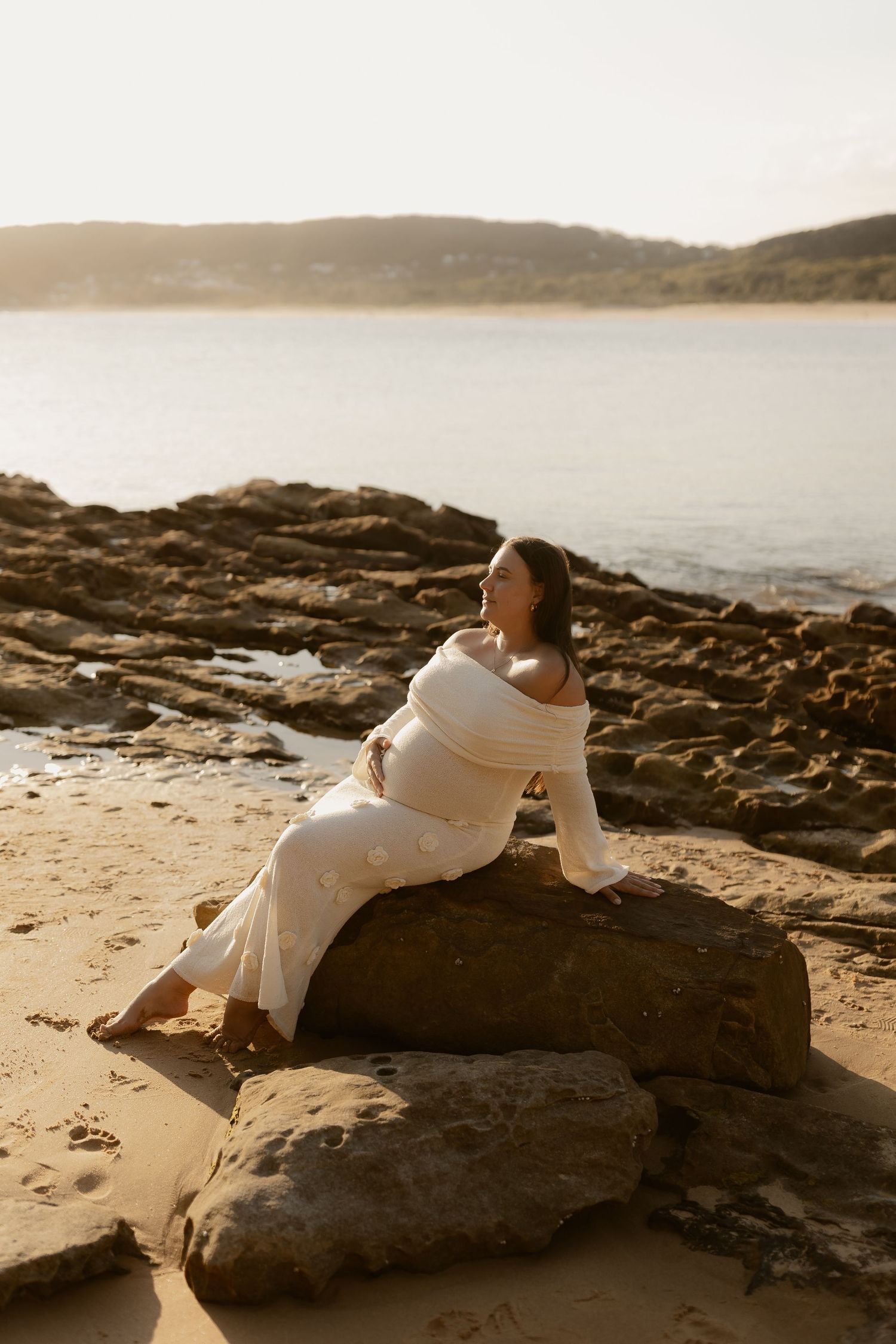 Artistic portrait of someone reclining on rocky coastal formations at golden hour.