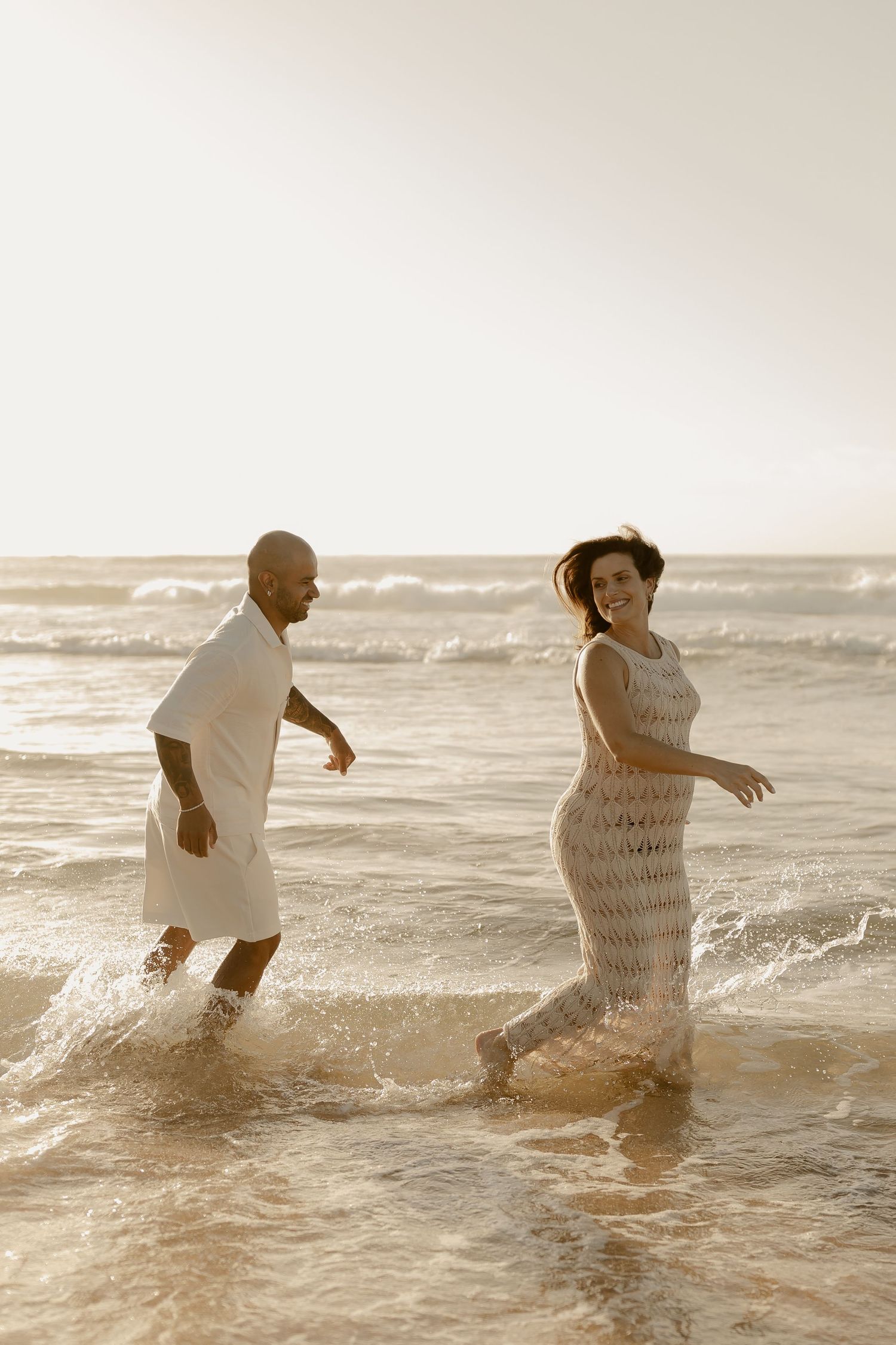 A couple playfully splashes in the ocean waves during a warm sunset, creating joyful moments together.