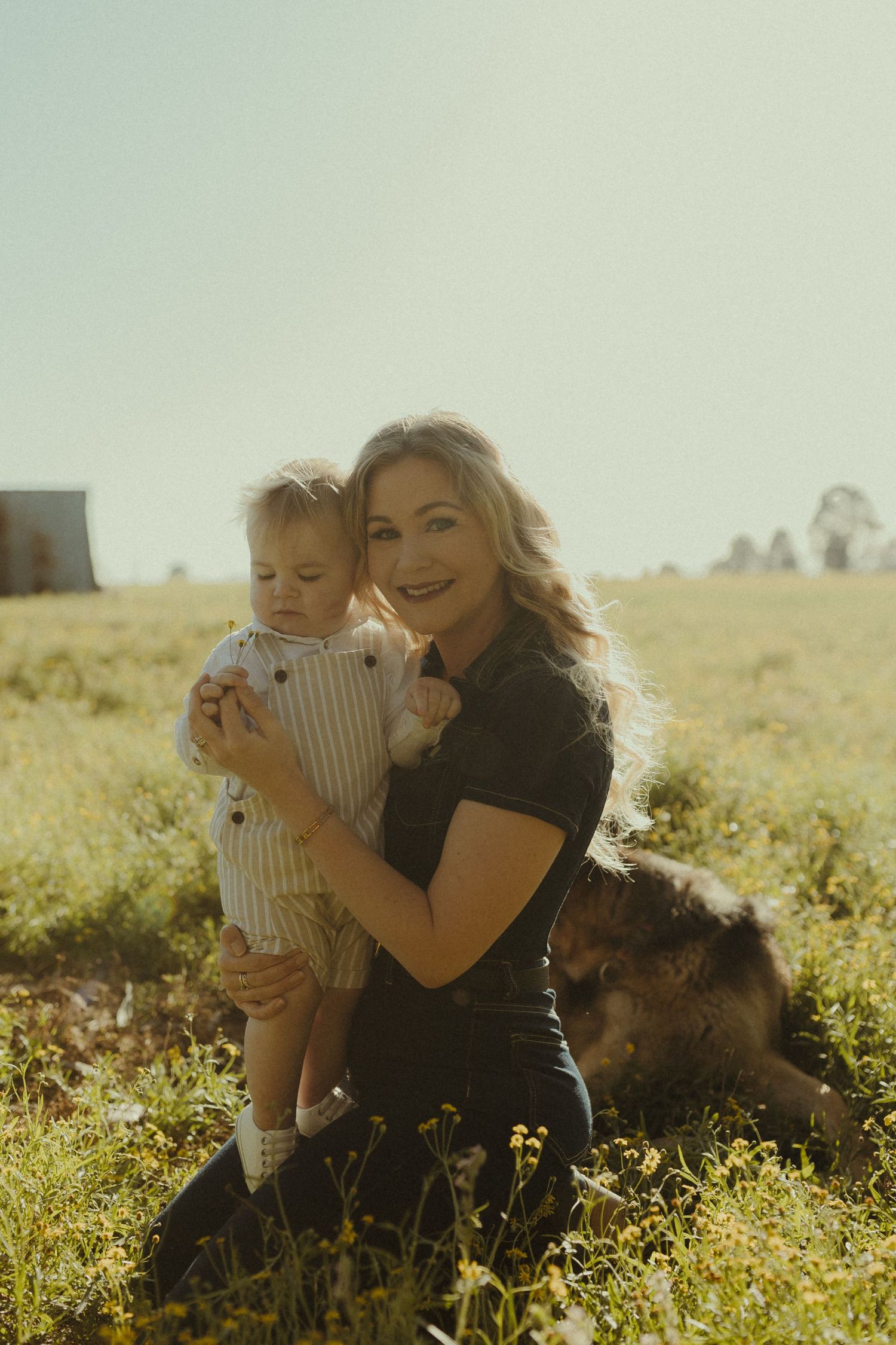 A parent and child sit together in a sunlit meadow filled with wildflowers during golden hour.