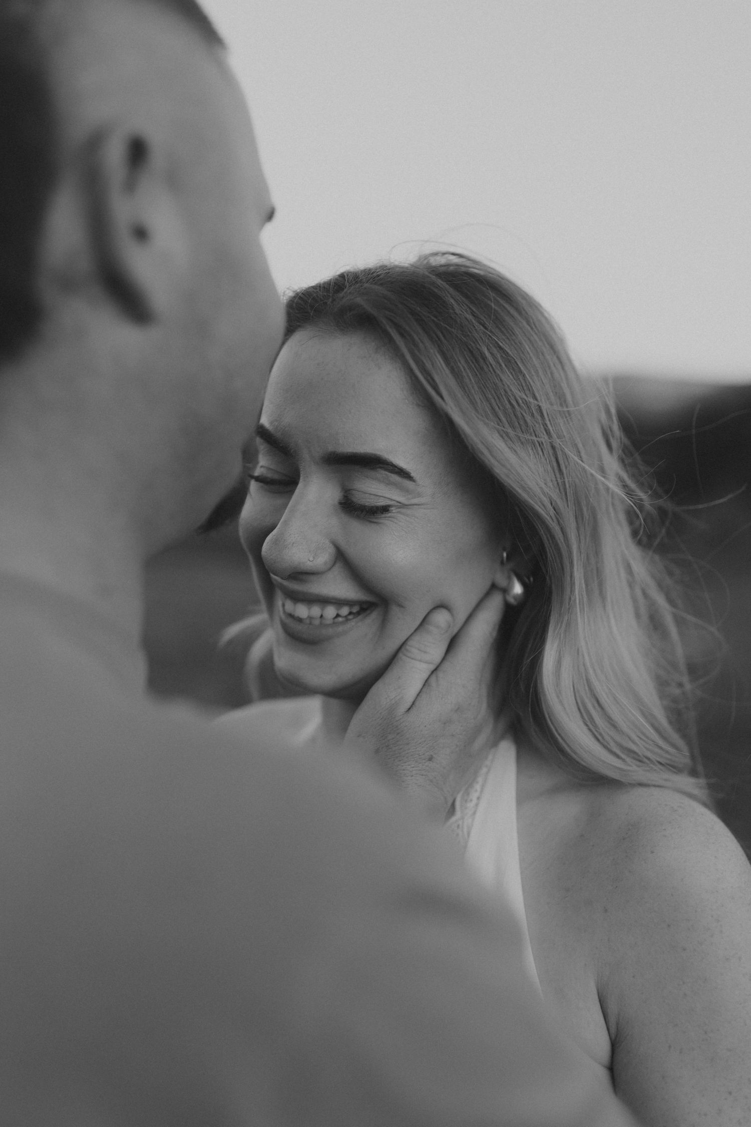 Black and white photo of a smiling woman with eyes closed as a man gently cups her face in a tender romantic moment.