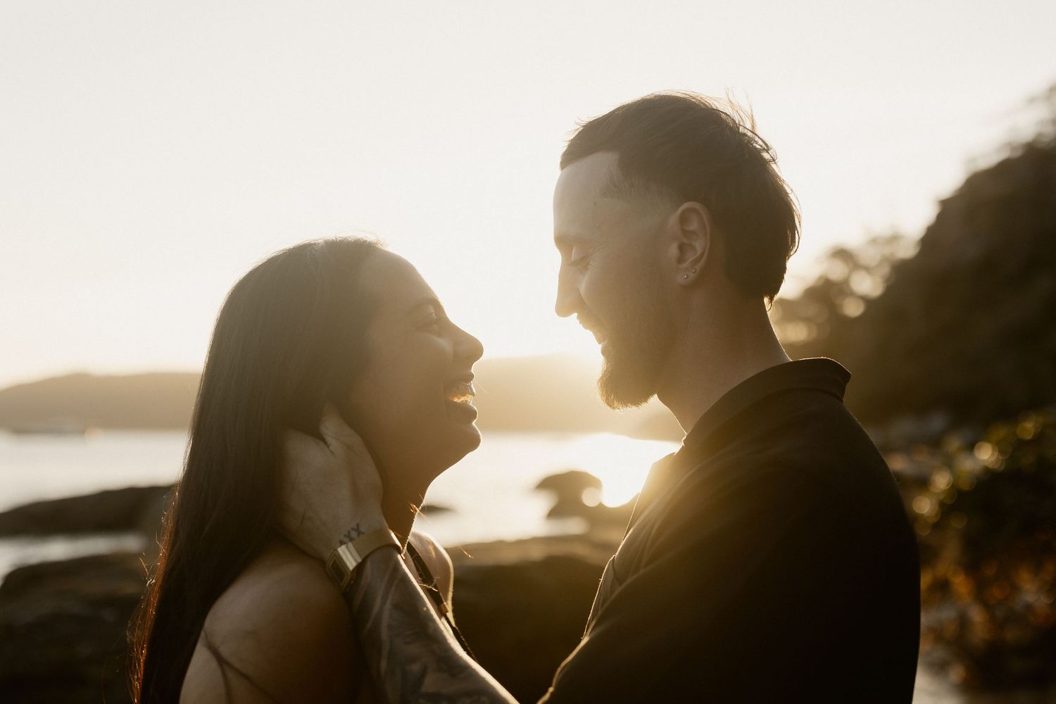 A backlit couple's silhouette shares an intimate moment against a sunset beach landscape.