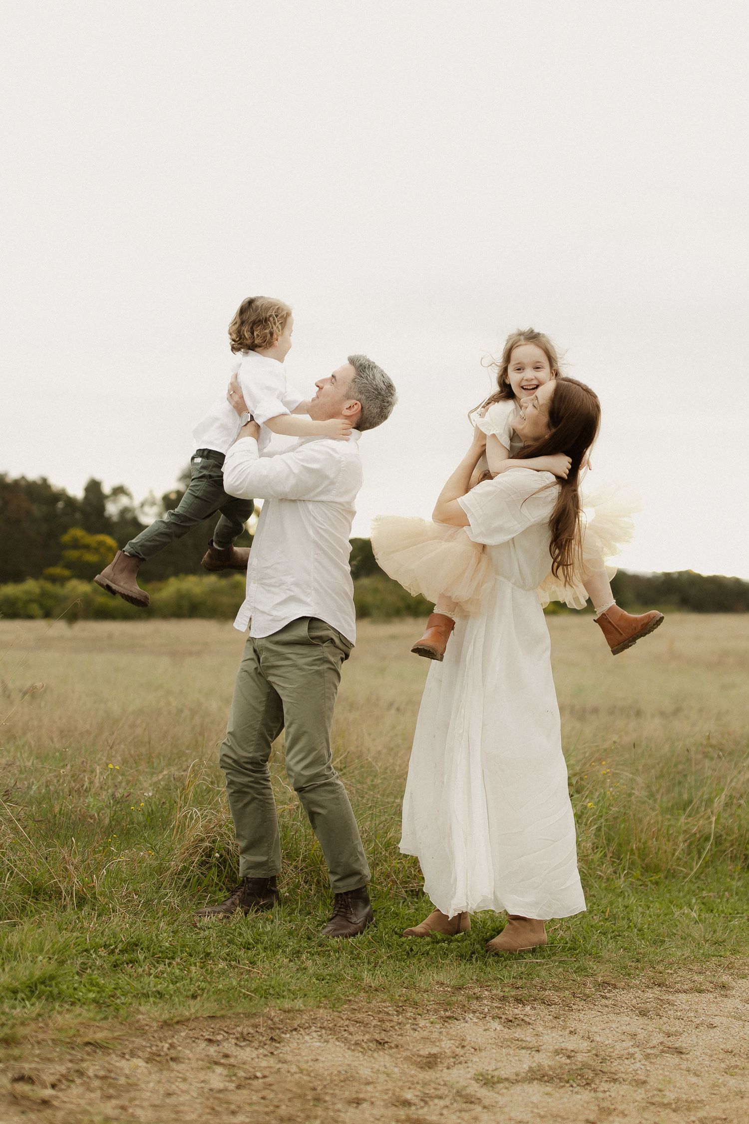 A playful couple dances together in a meadow wearing white and olive colored outfits.