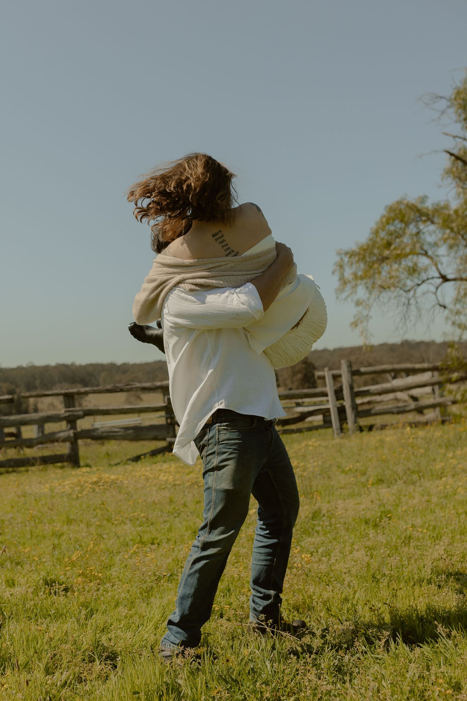 Joyful dance sequence in a sunny meadow with wooden fence in background.