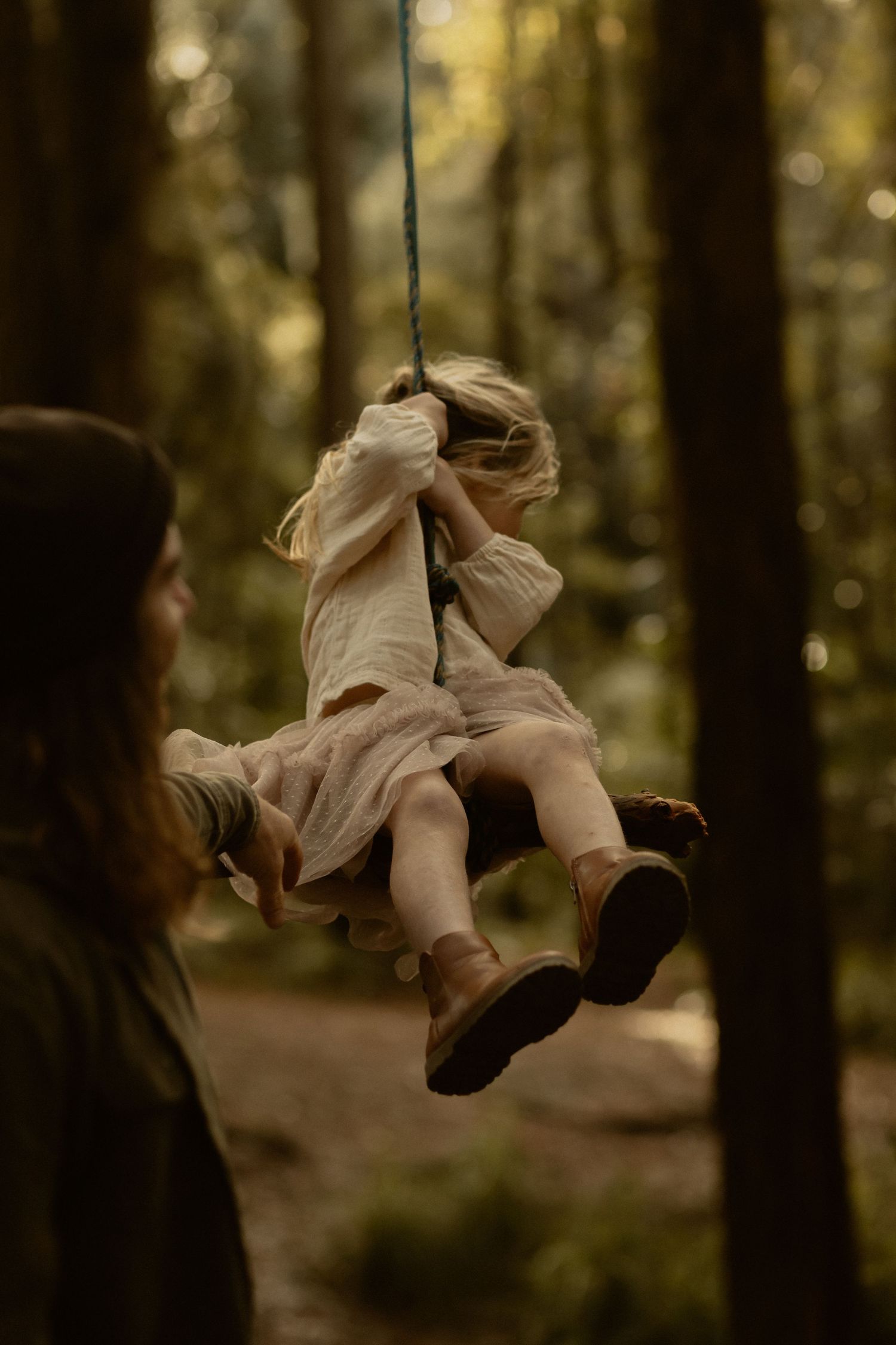 A child swings joyfully on a rope swing in a sun-dappled forest setting.