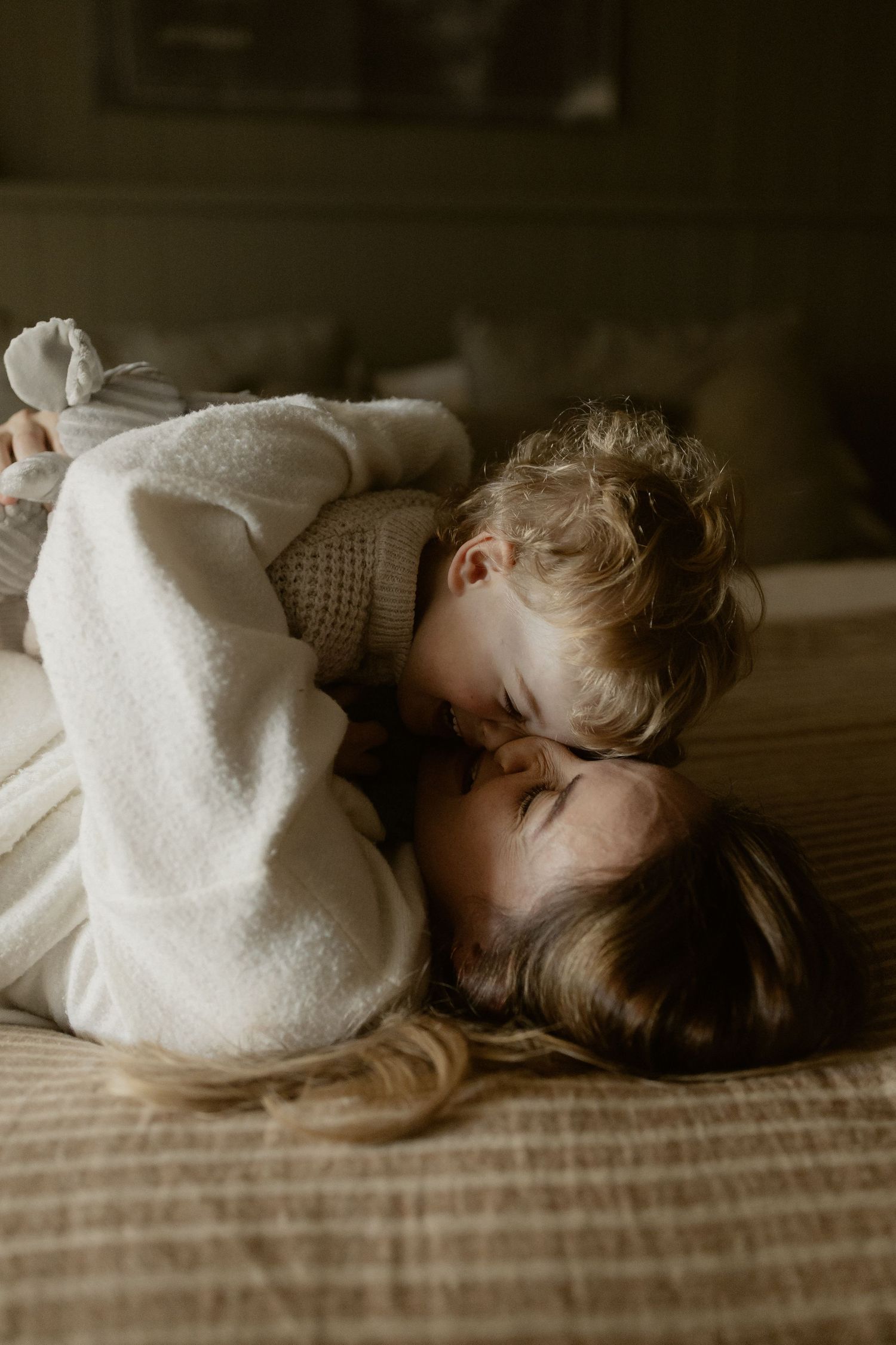 Tender moment captured in soft natural light on a comfortable bed with neutral tones.