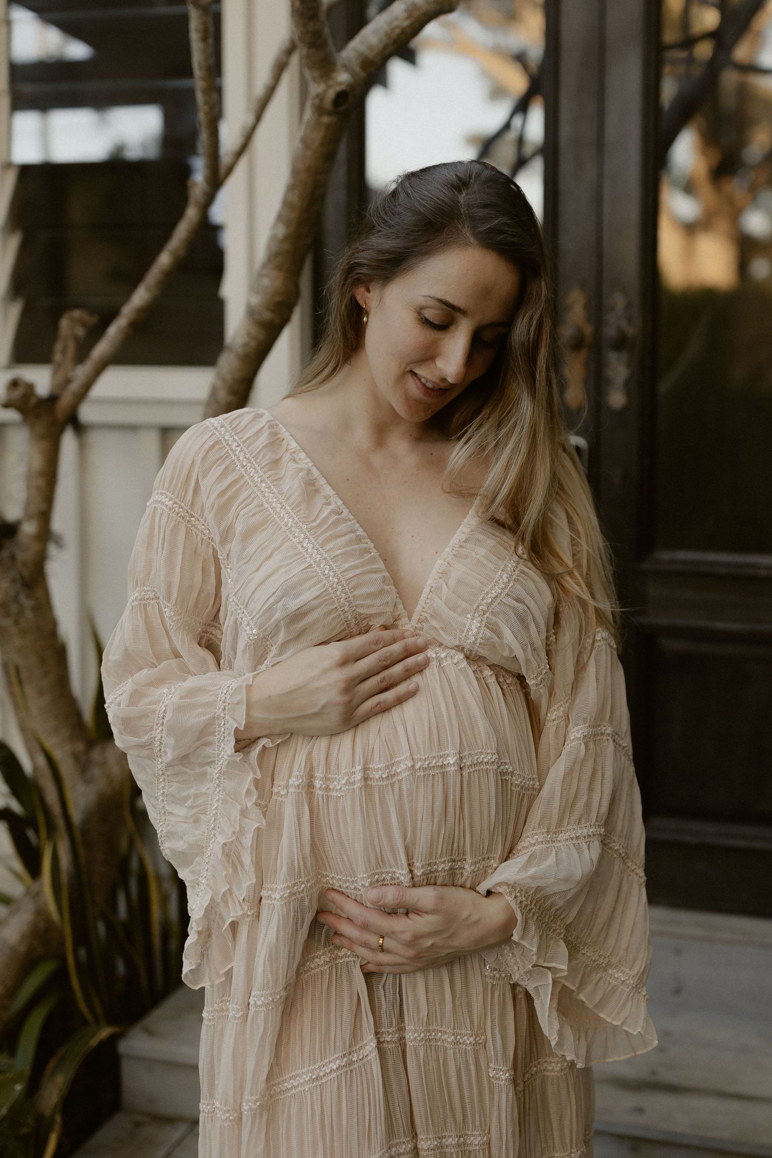A graceful figure in a flowy beige dress poses elegantly against a dark backdrop with natural light.