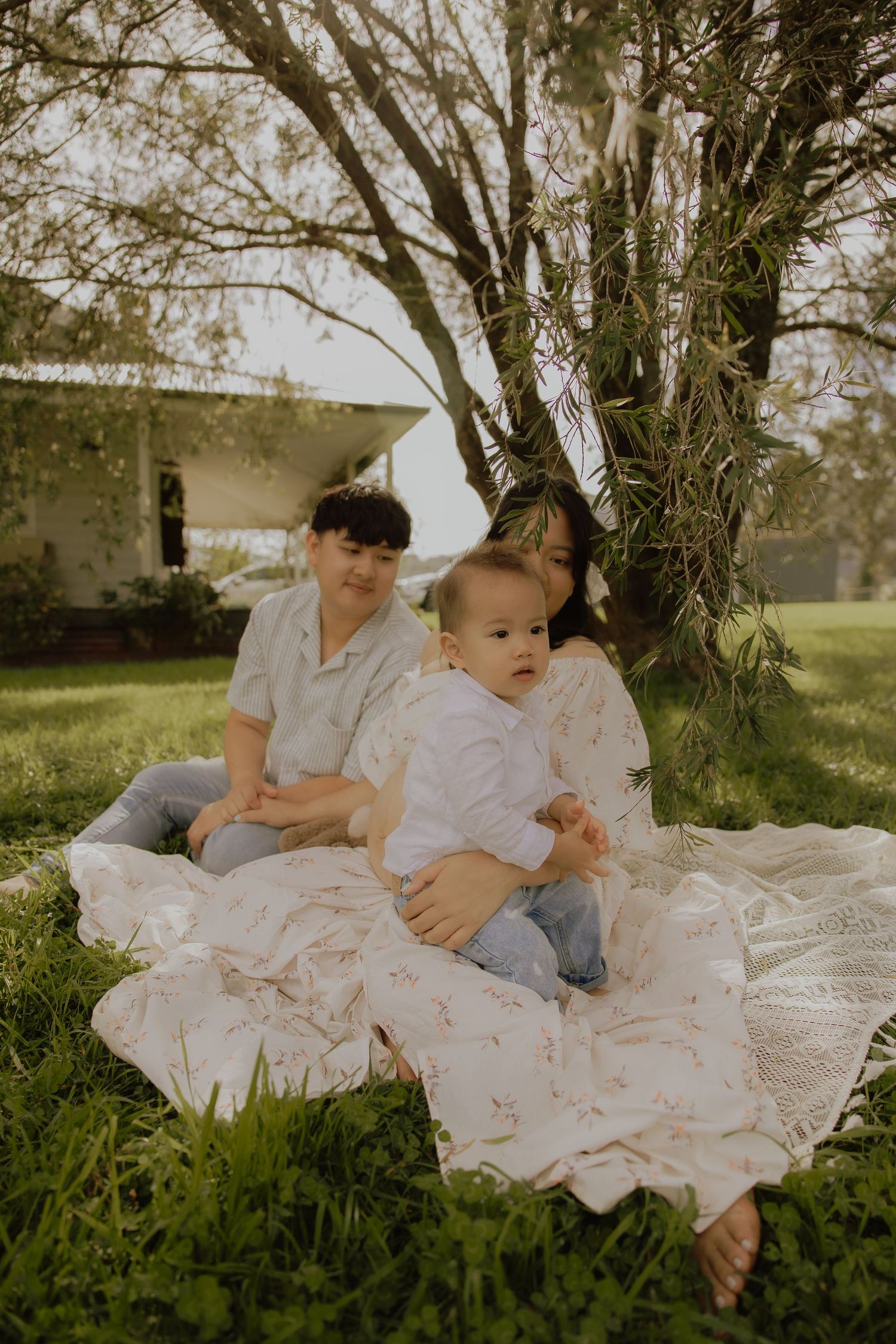 Family with baby sitting on floral blanket under tree in lush garden.