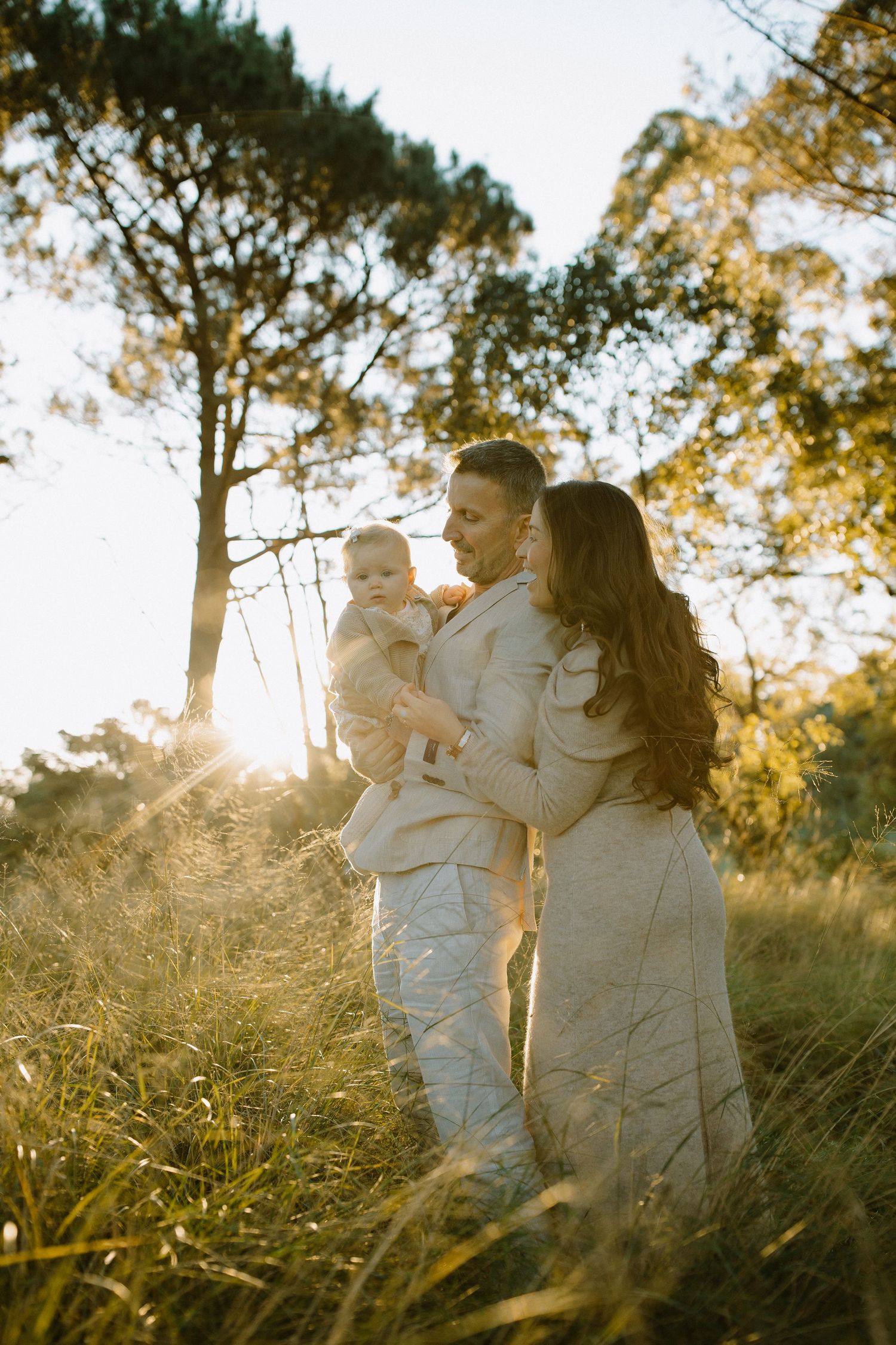 Family embracing in a sunlit field with tall pine trees at golden hour.
