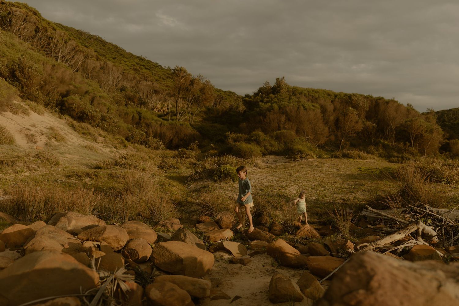 Two people exploring rocky coastal terrain under moody autumn skies.