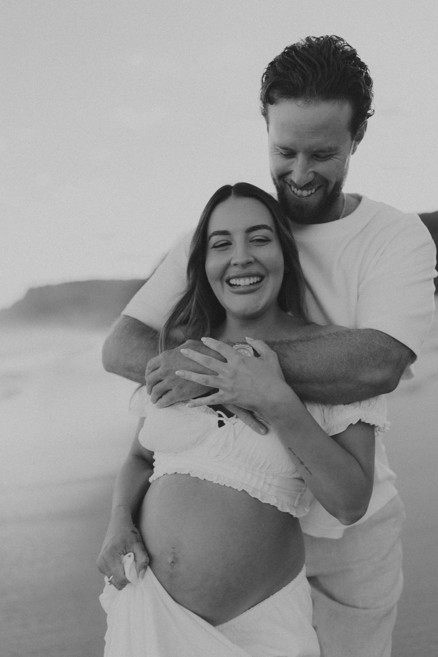 A couple embraces on the beach in a series of black and white candid photos showing playful affection.