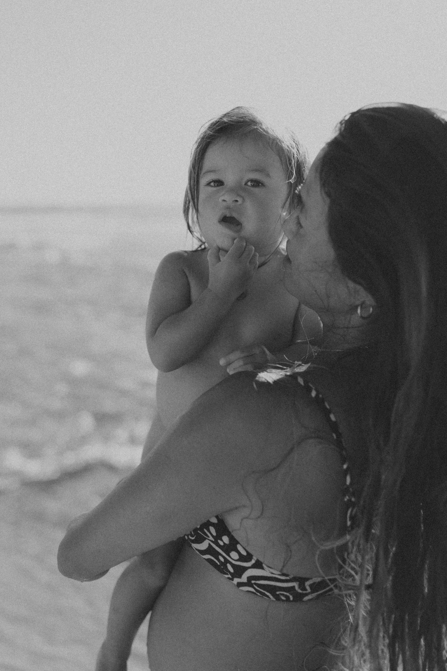 A tender moment between parent and baby against an ocean backdrop.
