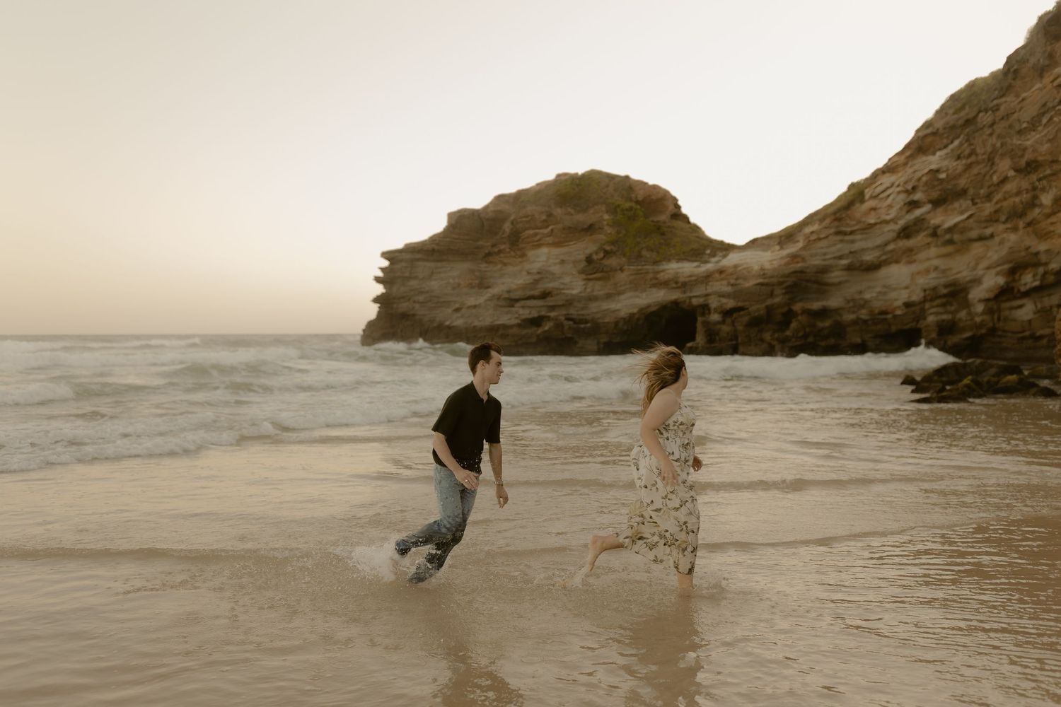 People enjoying a peaceful walk along a sandy beach with coastal cliffs at sunset.