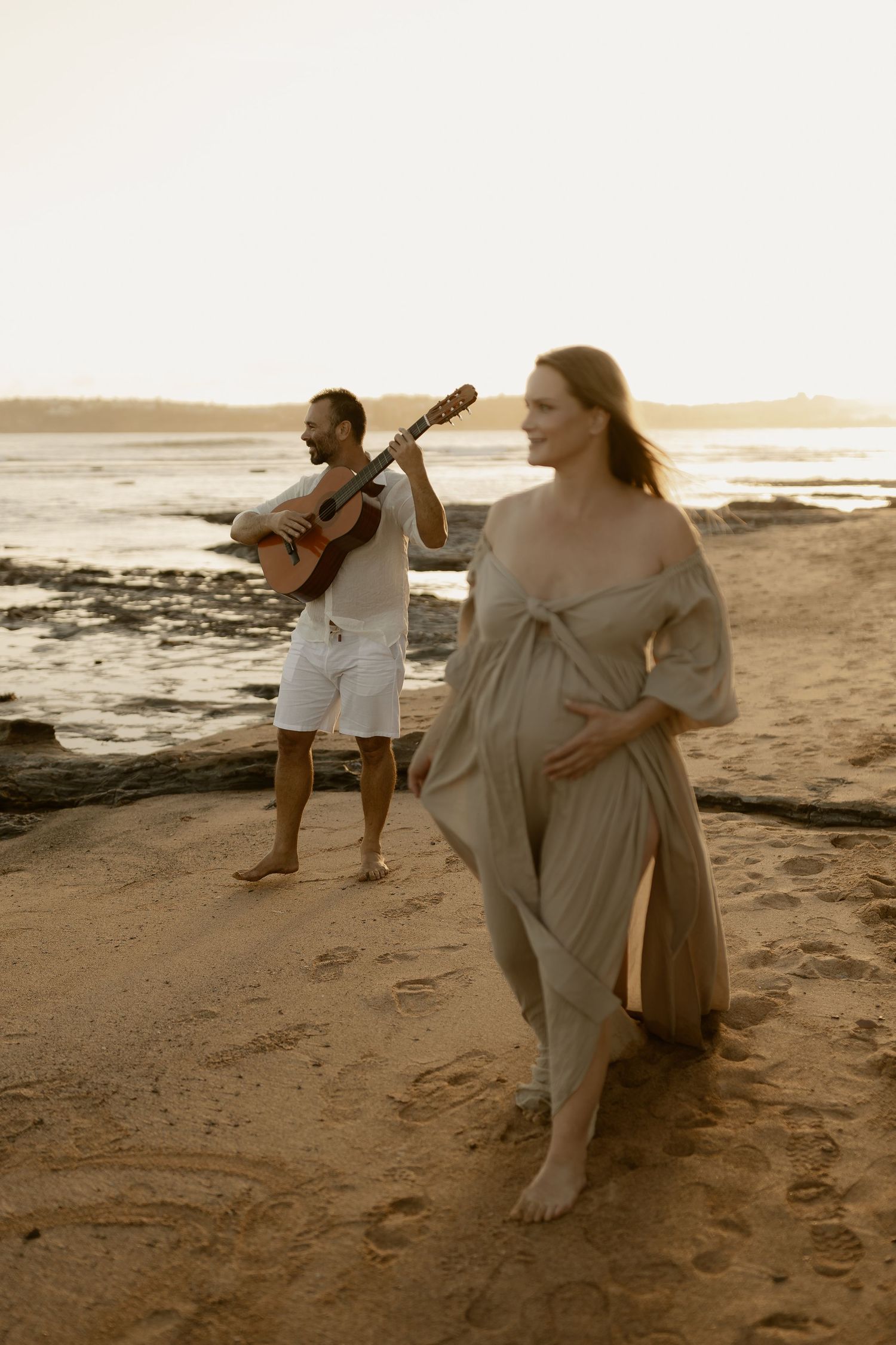 A couple dances together on a sandy beach during golden hour.
