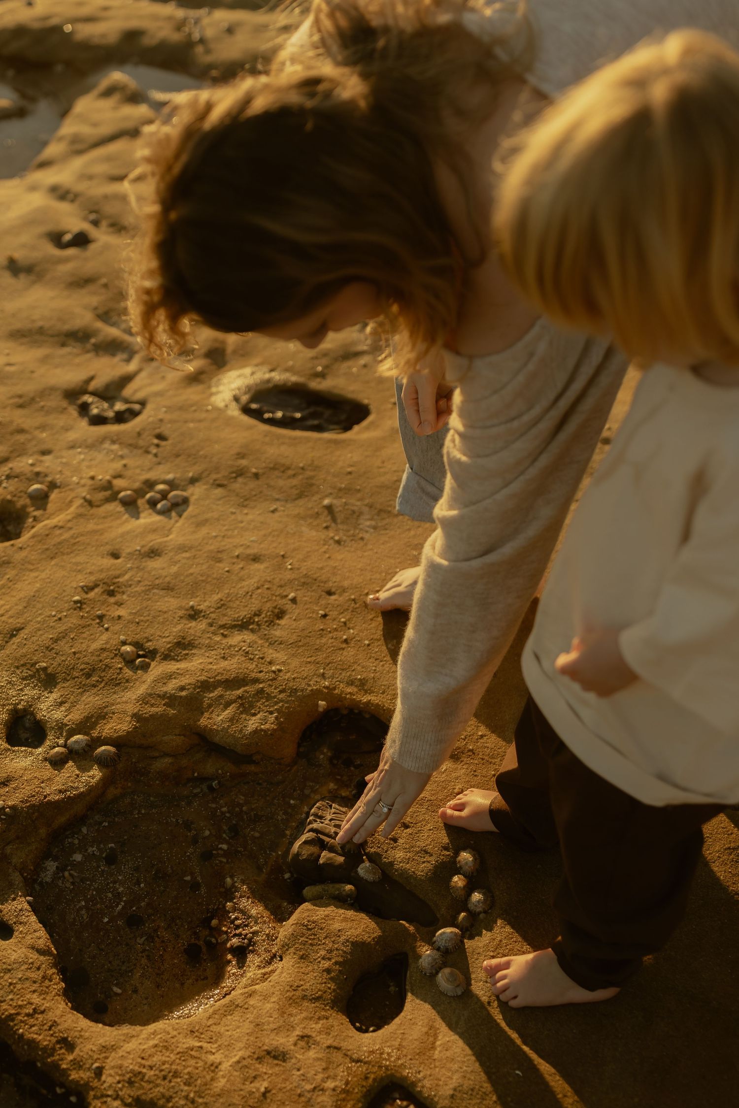 Two children playing with rocks and sand on a beach at sunset.