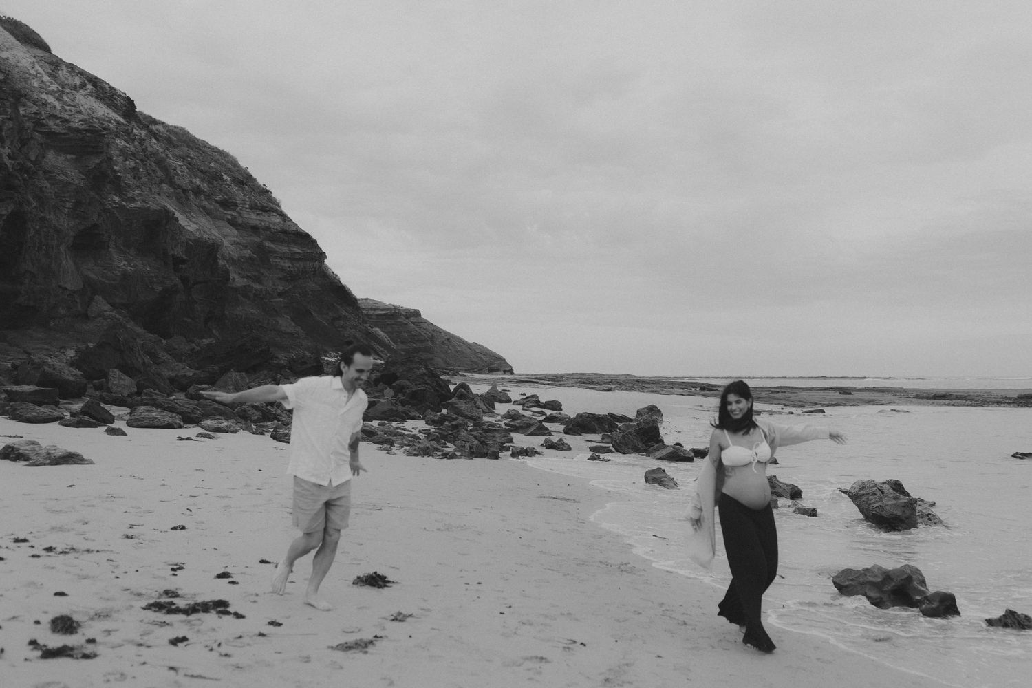 Couple walks along dramatic rocky coastline in black and white.
