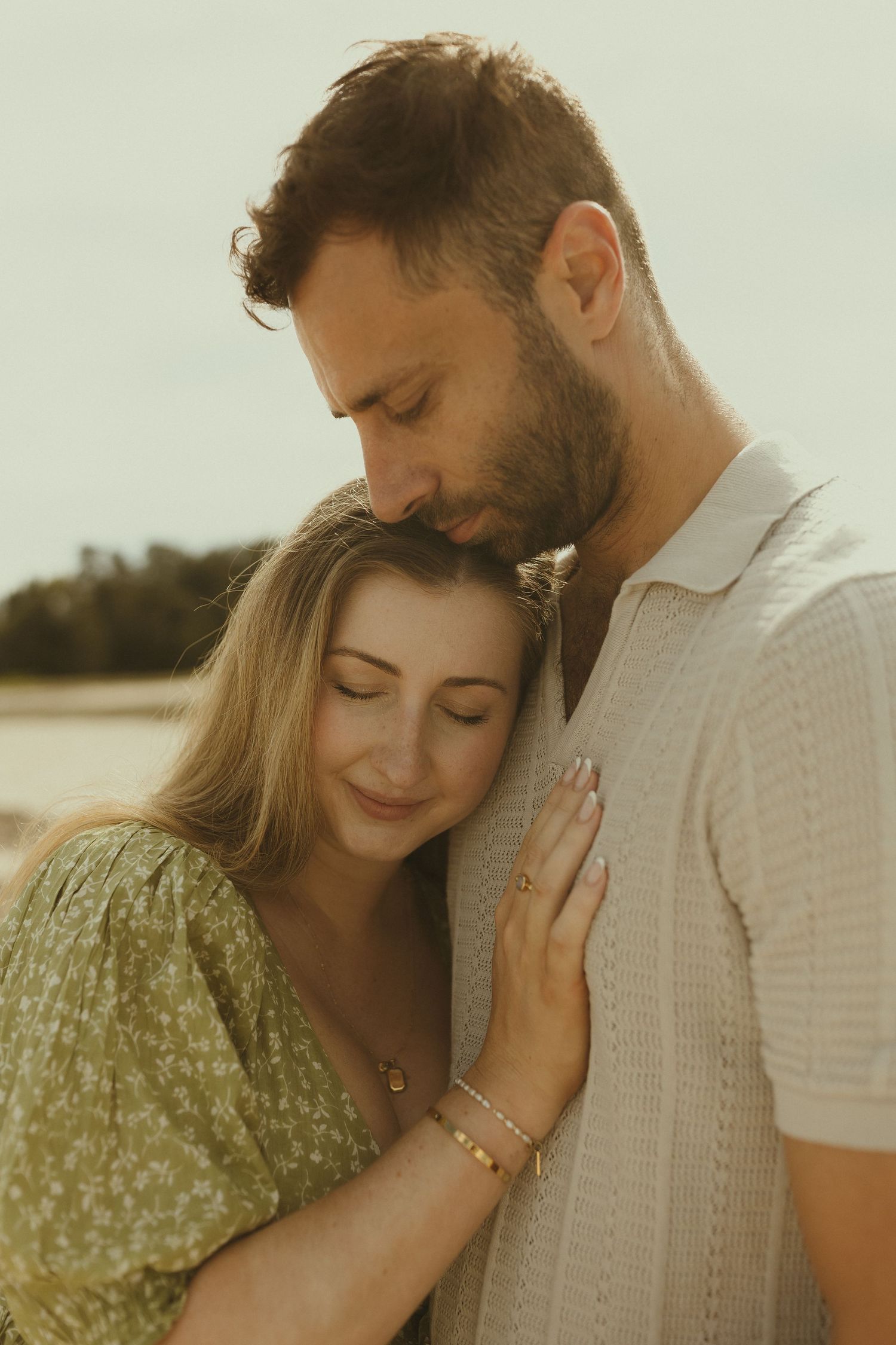 A couple shares intimate moments on the beach in warm sunlight wearing casual summer attire.