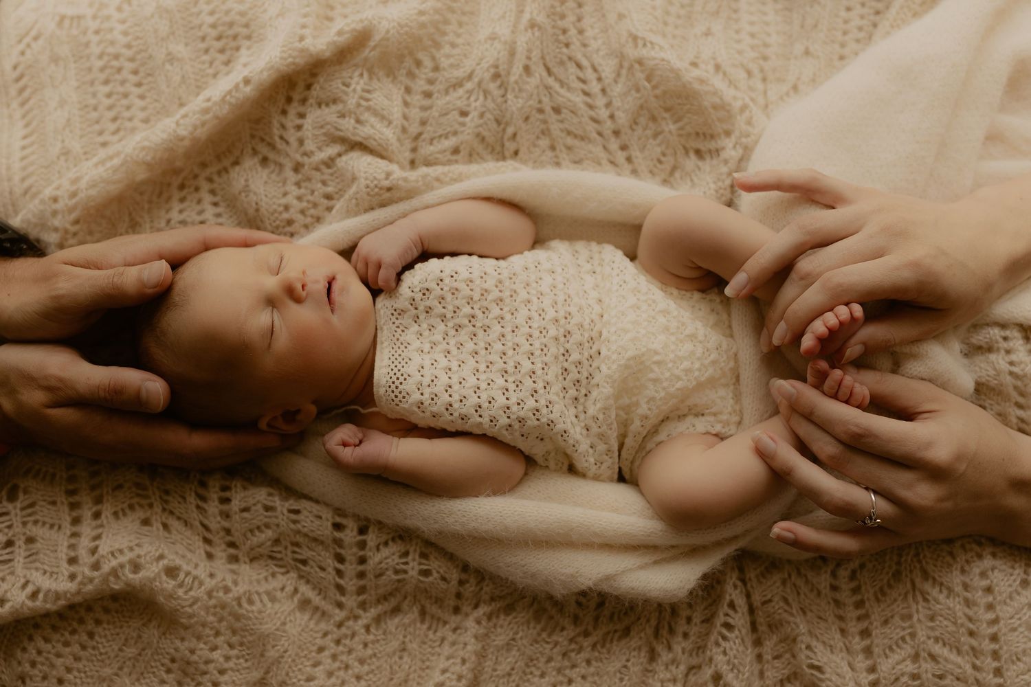 A series of sepia-toned photographs showing gentle hands cradling and holding a newborn baby in soft knit clothing.