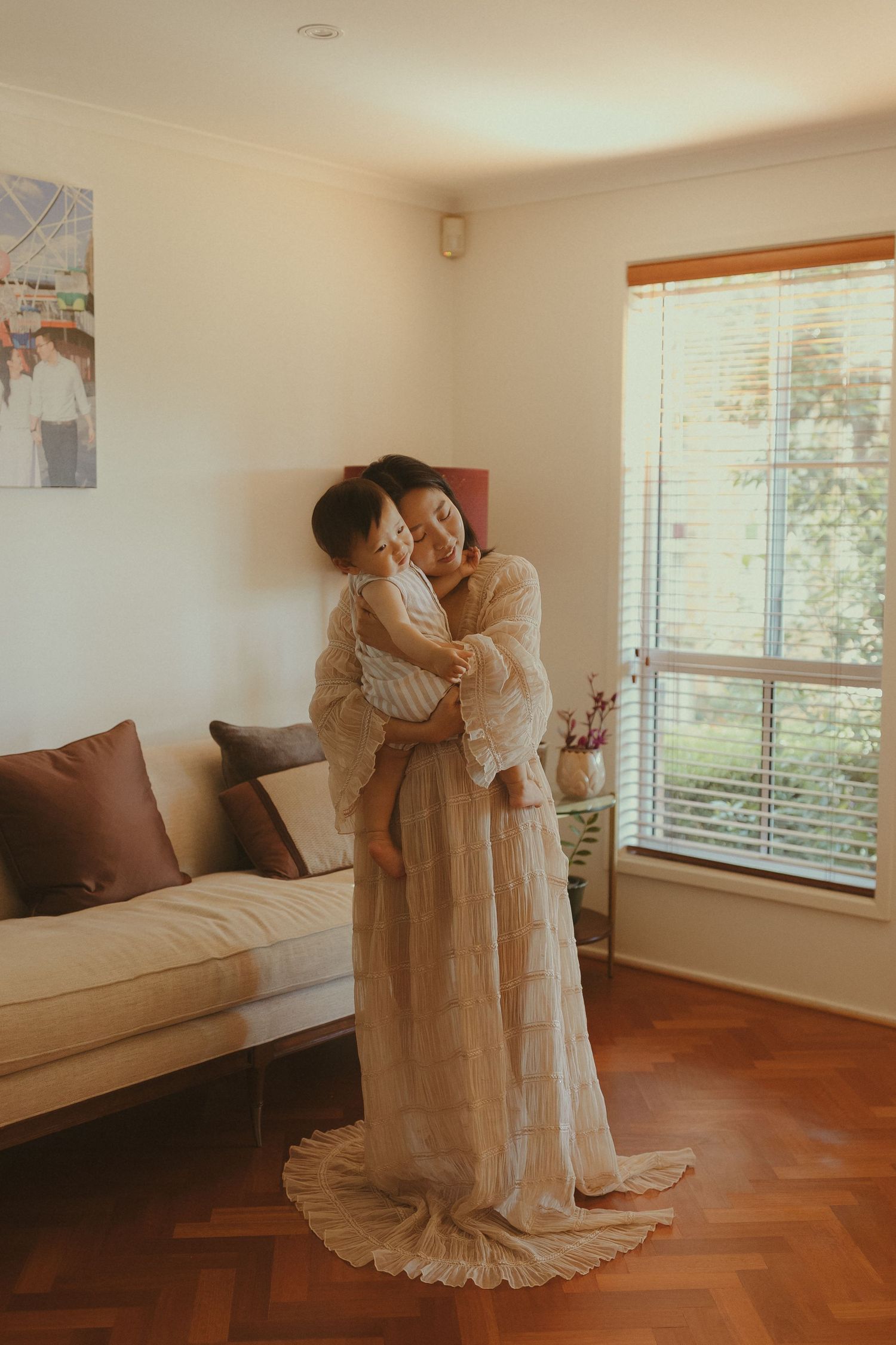 A tender moment captured in a living room with soft natural light streaming through window blinds.